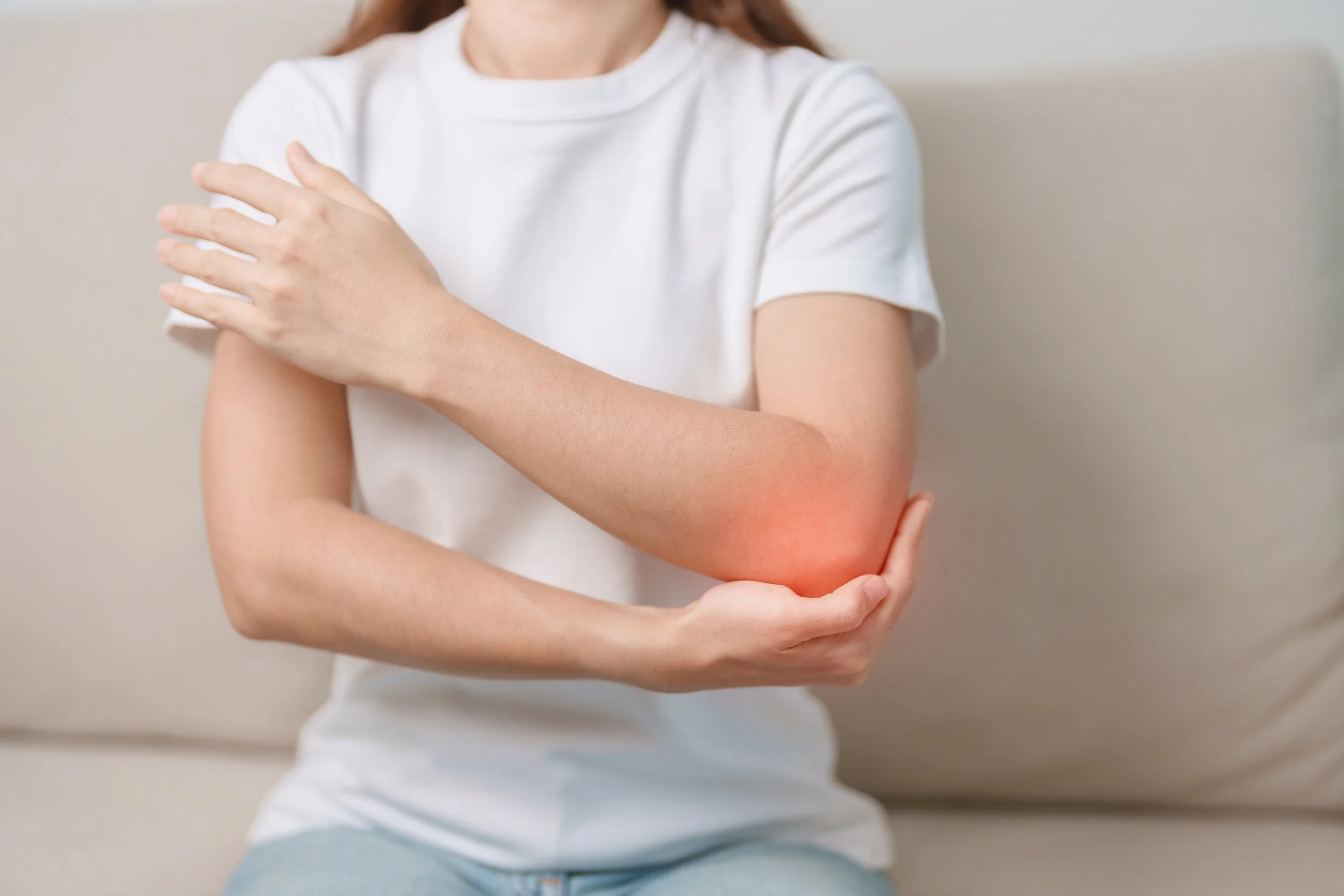 A woman in a white t-shirt clutching her painful elbow with a red glow indicator, seeking specialized physical therapy in Manhattan.