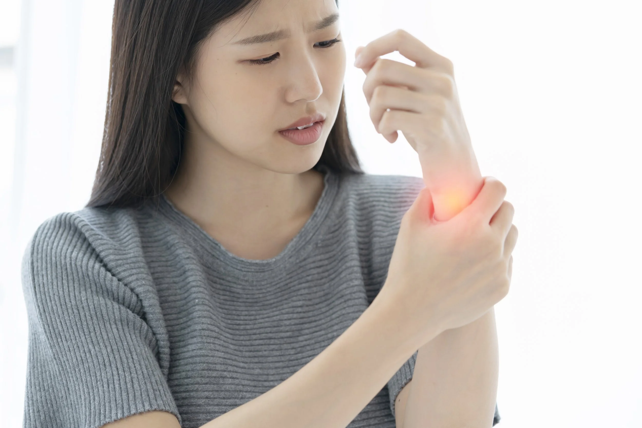 A woman clutching her painful wrist with a red pain indicator, seeking physical therapy for carpal tunnel or hand injuries at Signature PT in Manhattan.