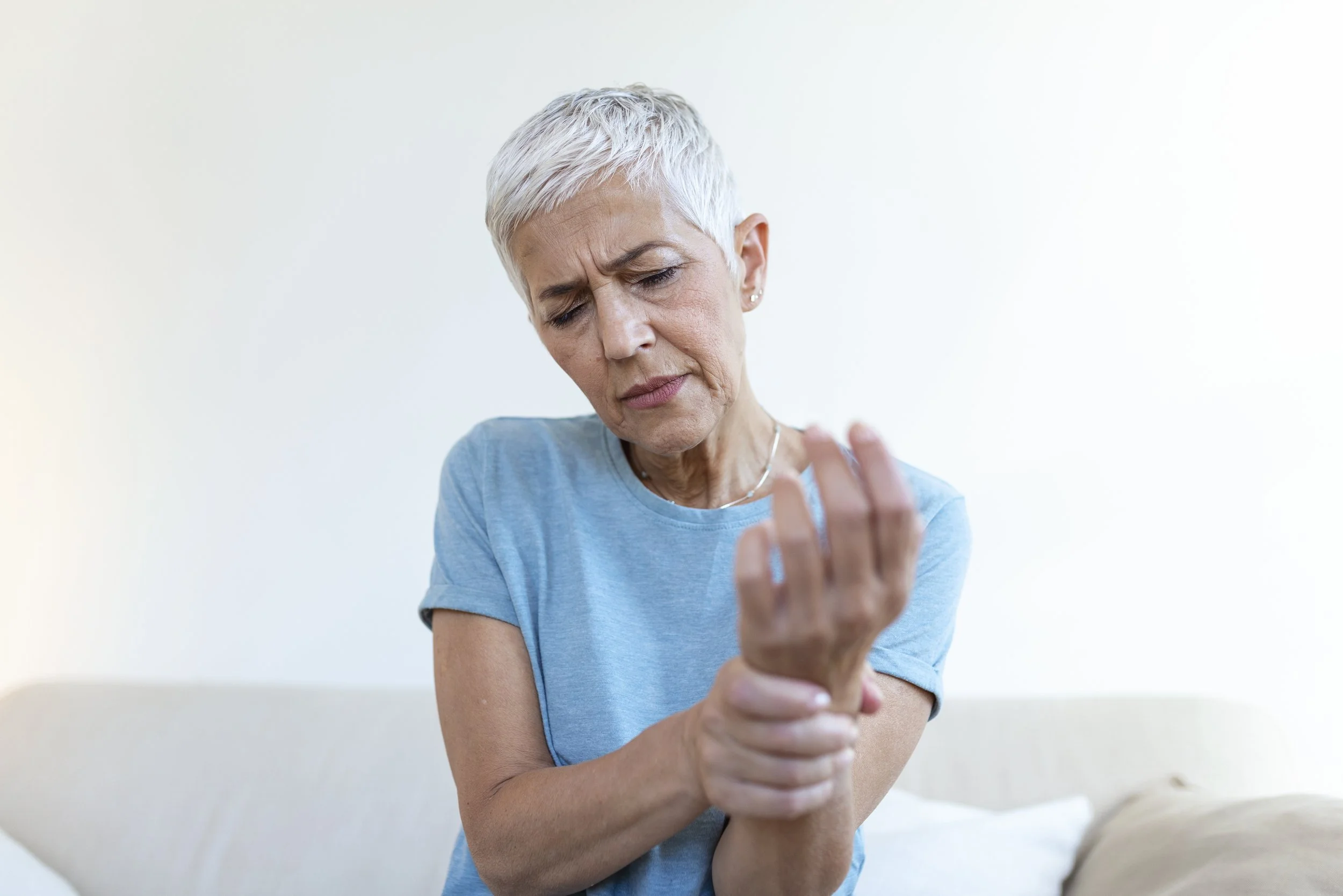 An older woman with short gray hair suffering from severe wrist and hand joint pain (arthritis), seeking expert physical therapy in Washington Heights, Manhattan at Signature PT.