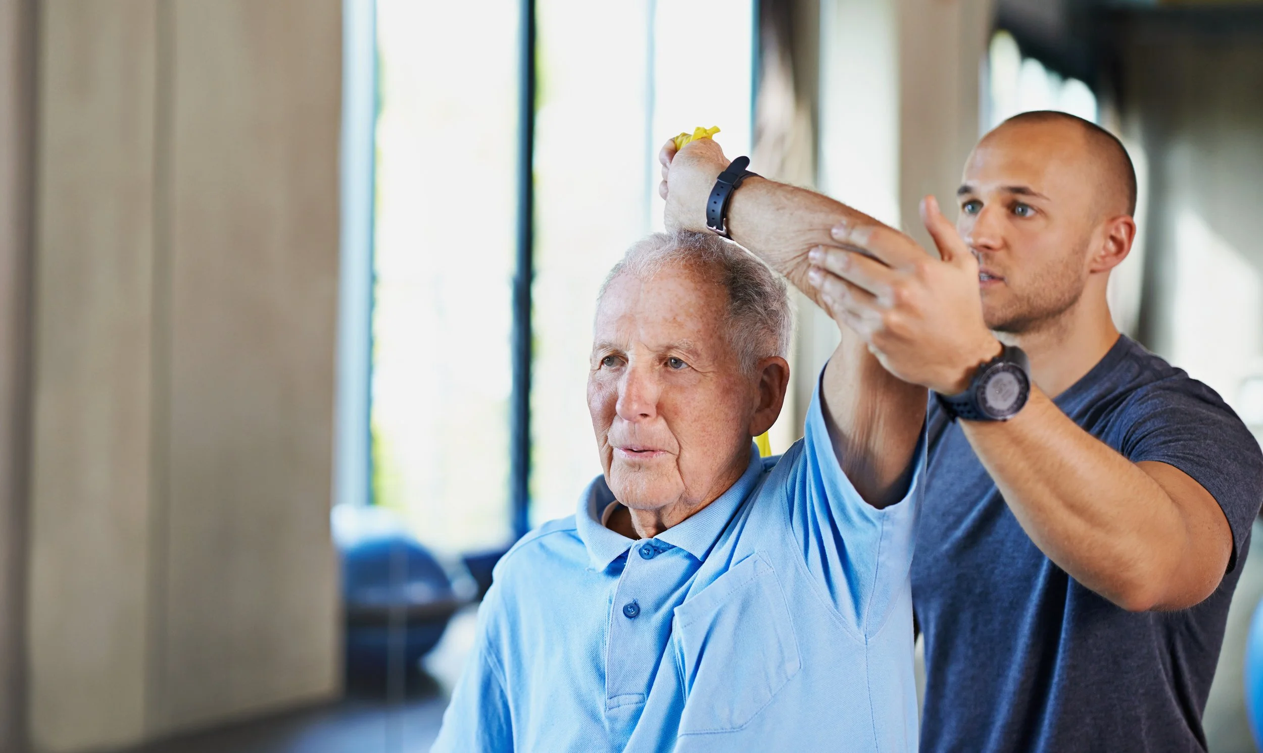 A professional male physical therapist at Signature PT providing hands-on upper body rehabilitation and neuro-motor training for a stroke survivor in Manhattan.