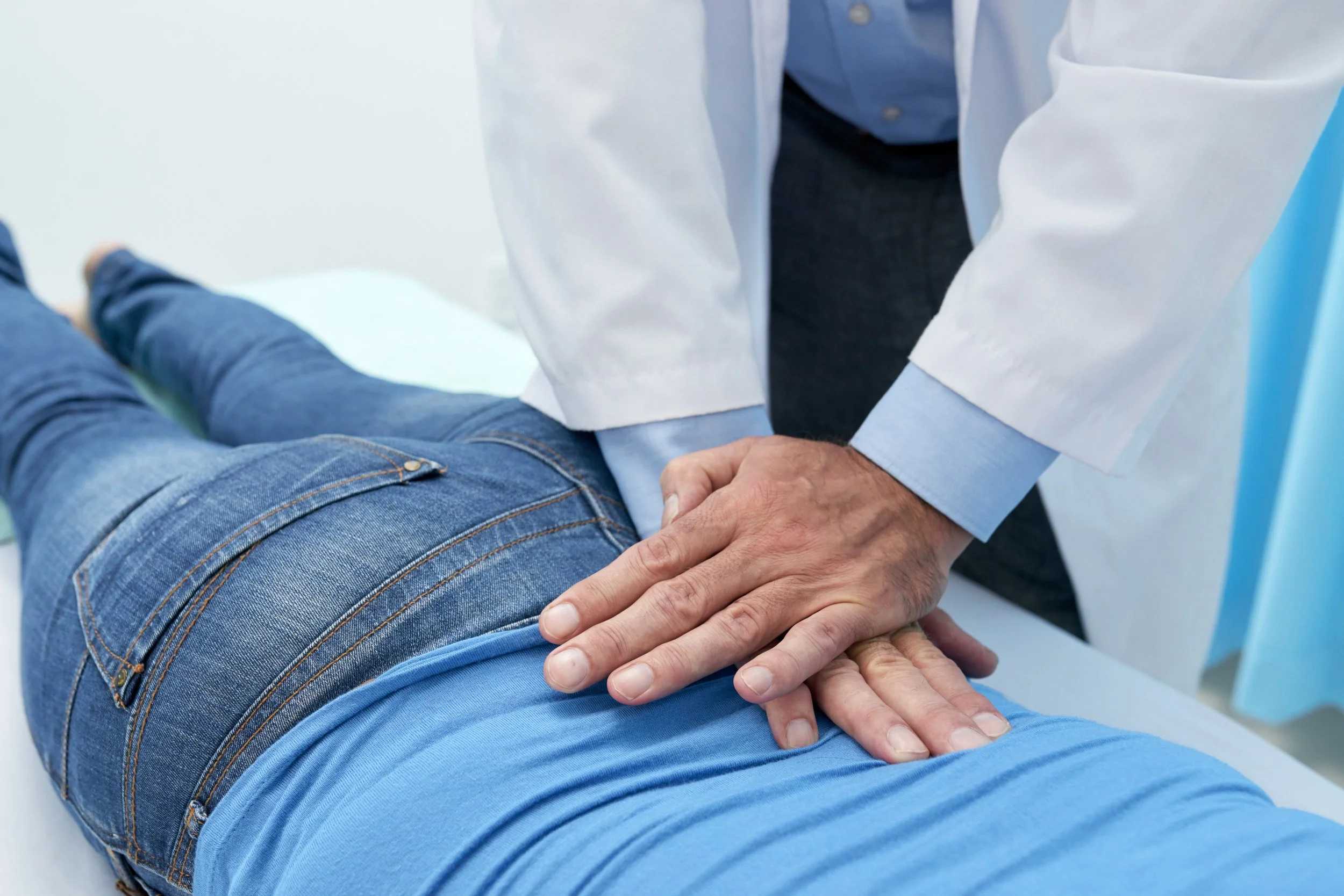 A doctor in a white coat performing manual spinal manipulation and pressure point therapy on a patient's lower back to relieve chronic lumbago.