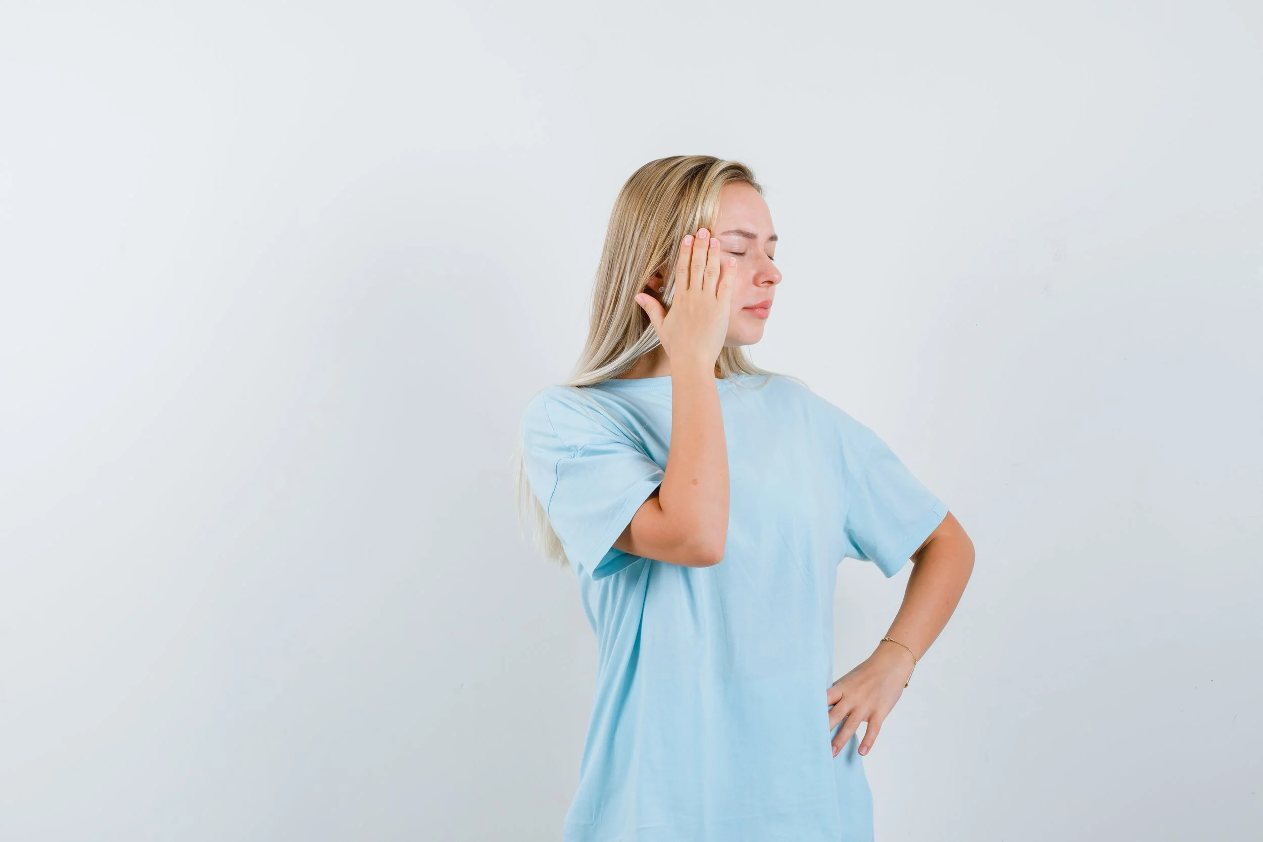 A woman holding her temple with eyes closed, experiencing nerve pain or a neurological symptoms, seeking specialized physical therapy at Signature PT in Manhattan.
