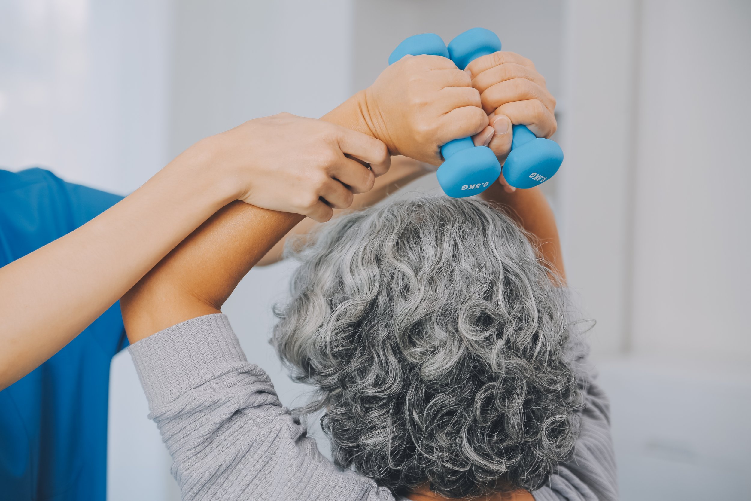 A stroke patient performing overhead dumbbell strengthening exercises under the careful guidance of a physical therapist to restore muscle function and coordination.