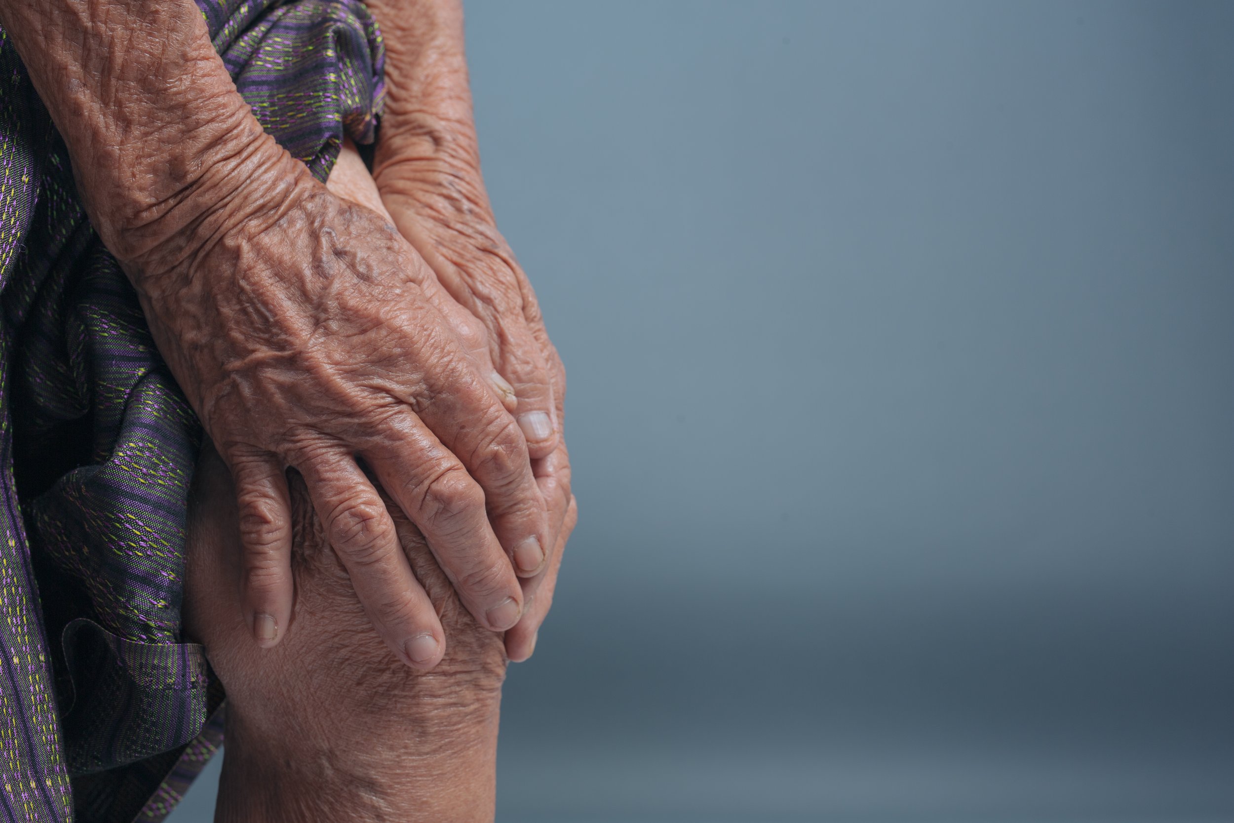 Close-up of an elderly patient’s weathered hands clutching a painful knee, seeking long-term joint relief at Signature PT in Manhattan.