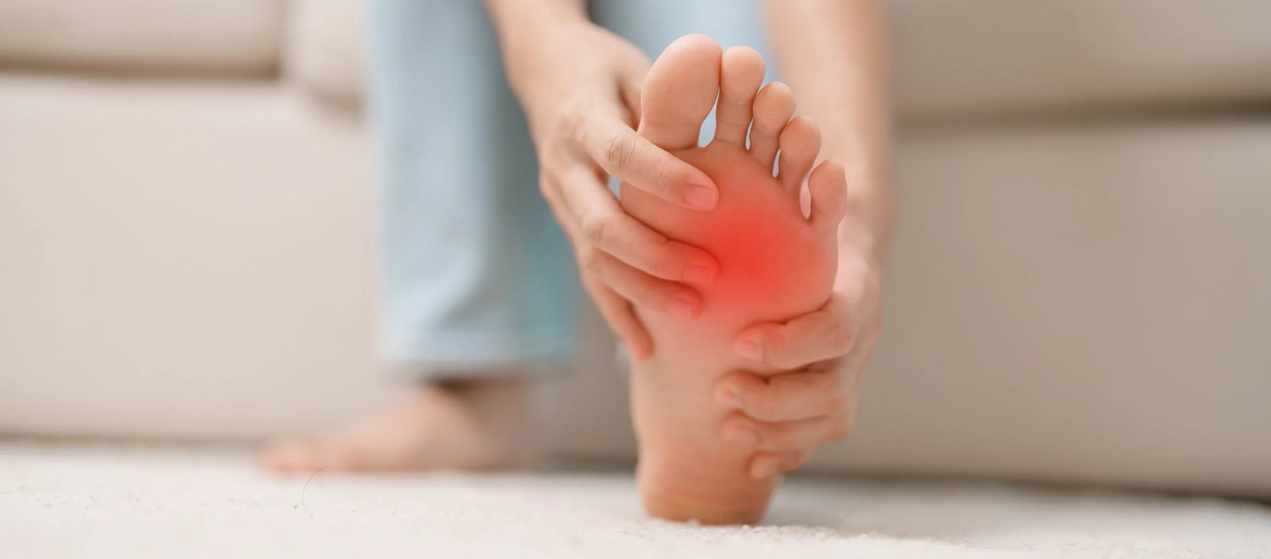 Close-up of a person holding their bare foot with a vibrant red pain indicator on the sole, seeking physical therapy for generalized foot relief in Manhattan.