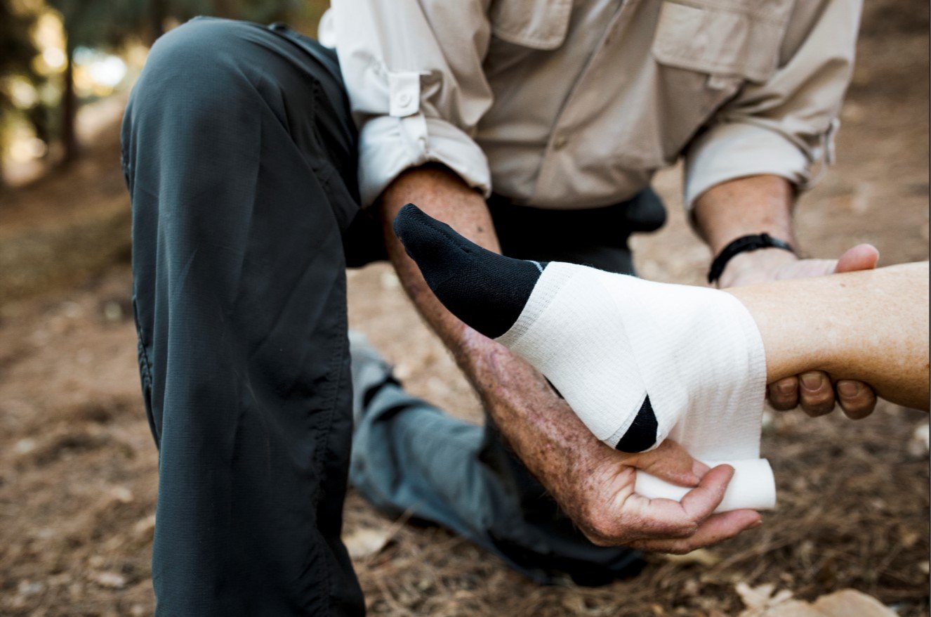 Close-up of a worker receiving first aid and a compression wrap on a sprained ankle, illustrating common workplace injury symptoms and acute trauma.