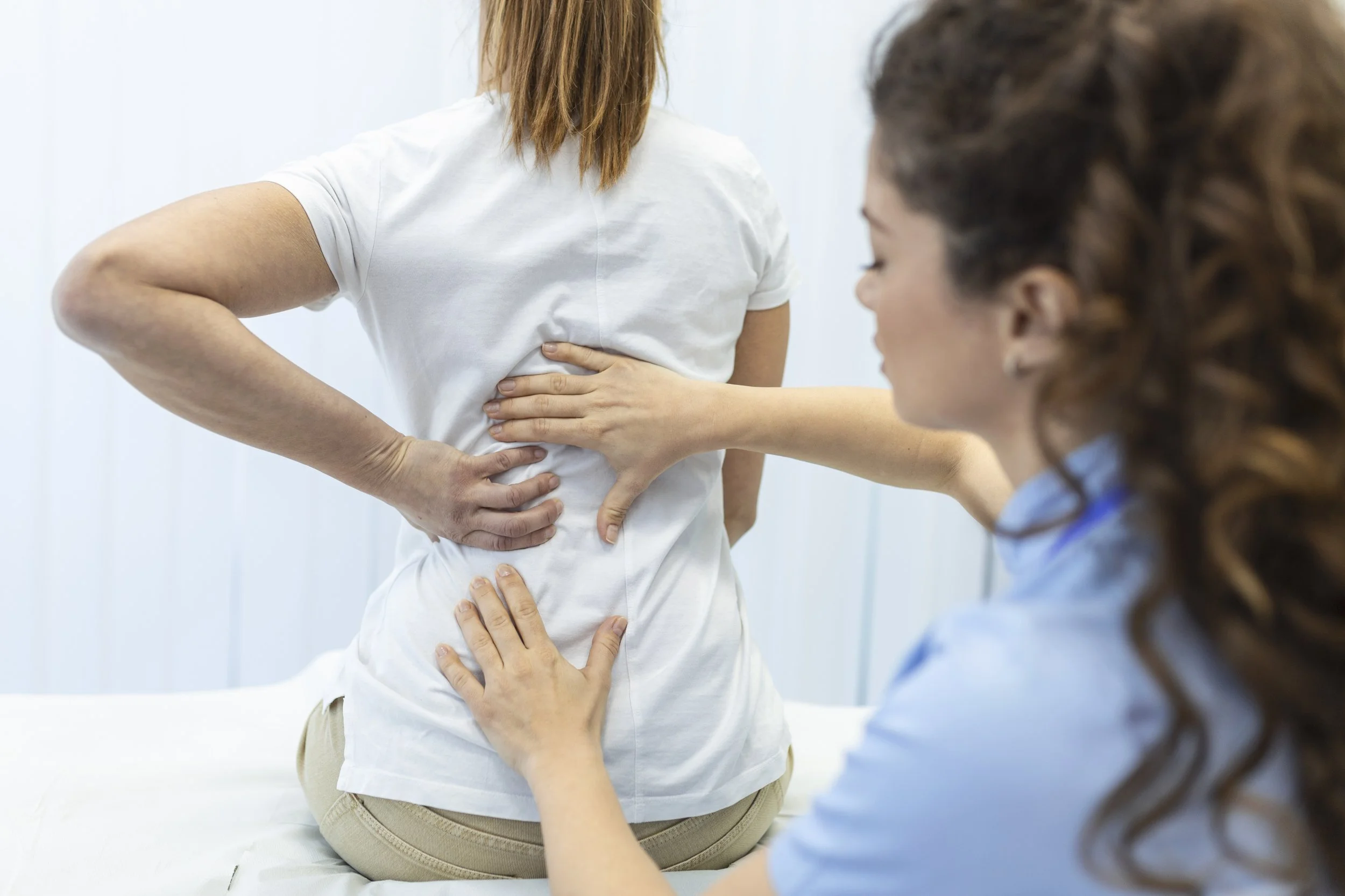 A physical therapist at Signature PT performing a manual spinal assessment and alignment check on a patient to treat scoliosis and spine deformation.