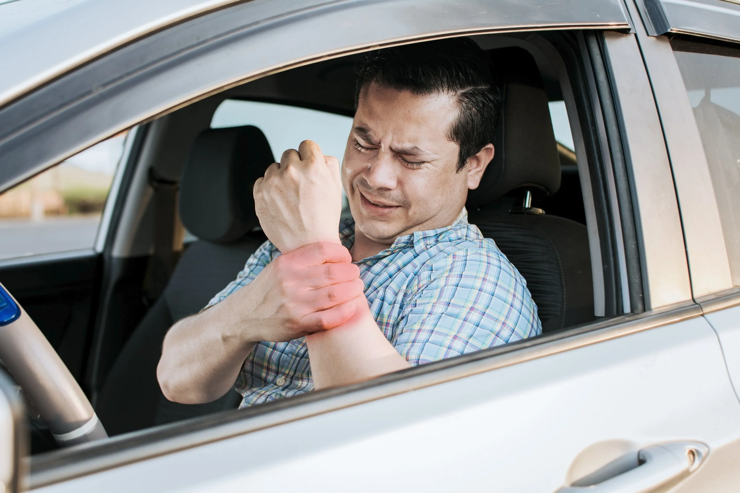 Close-up of a person sitting in a car seat, clutching their hip and midsection with a red pain indicator, illustrating symptoms of whiplash and torso trauma from a car accident.