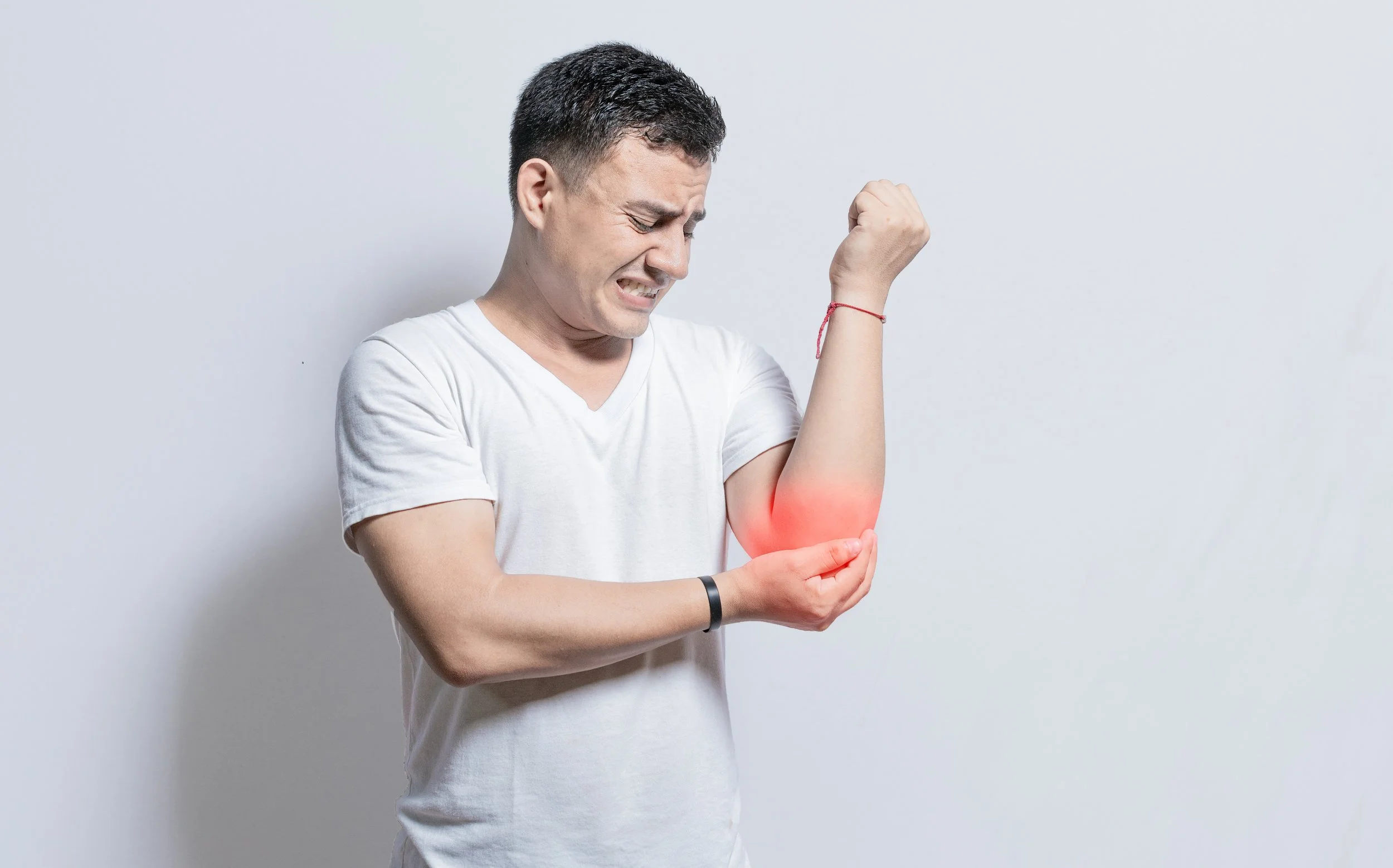 A man in a white t-shirt clutching his painful elbow with a red pain indicator, seeking physical therapy for tennis elbow at Signature PT in Manhattan.