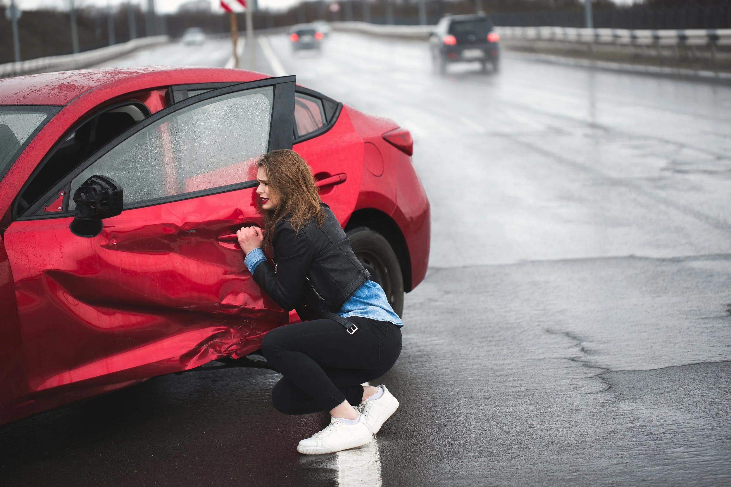A woman in distress near a red car after an accident, seeking physical therapy for whiplash and auto-related injuries at Signature PT in Manhattan.