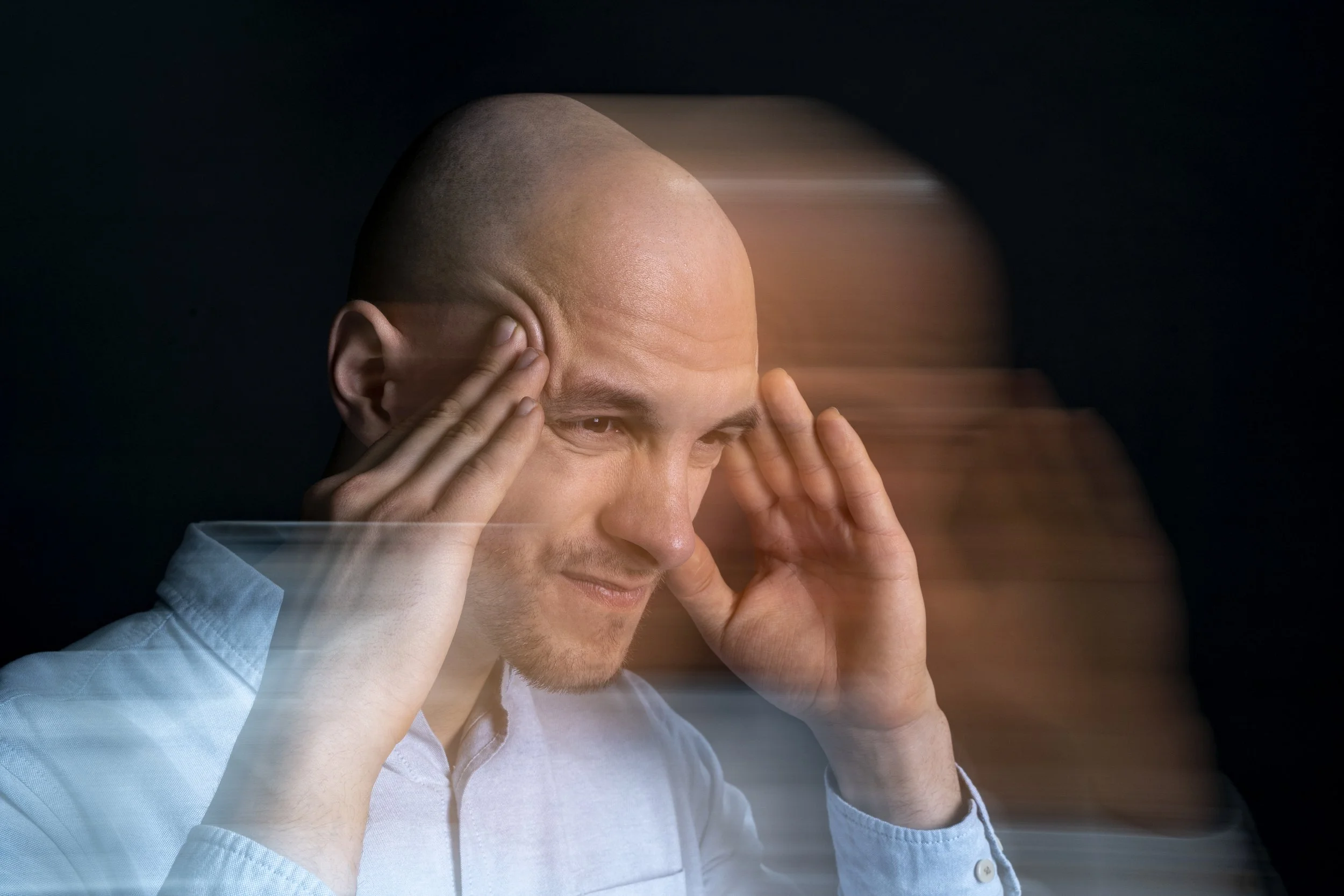 A man holding his temples with a motion blur effect, representing the sensory disorientation, dizziness, and shooting nerve pain of neurological disorders.