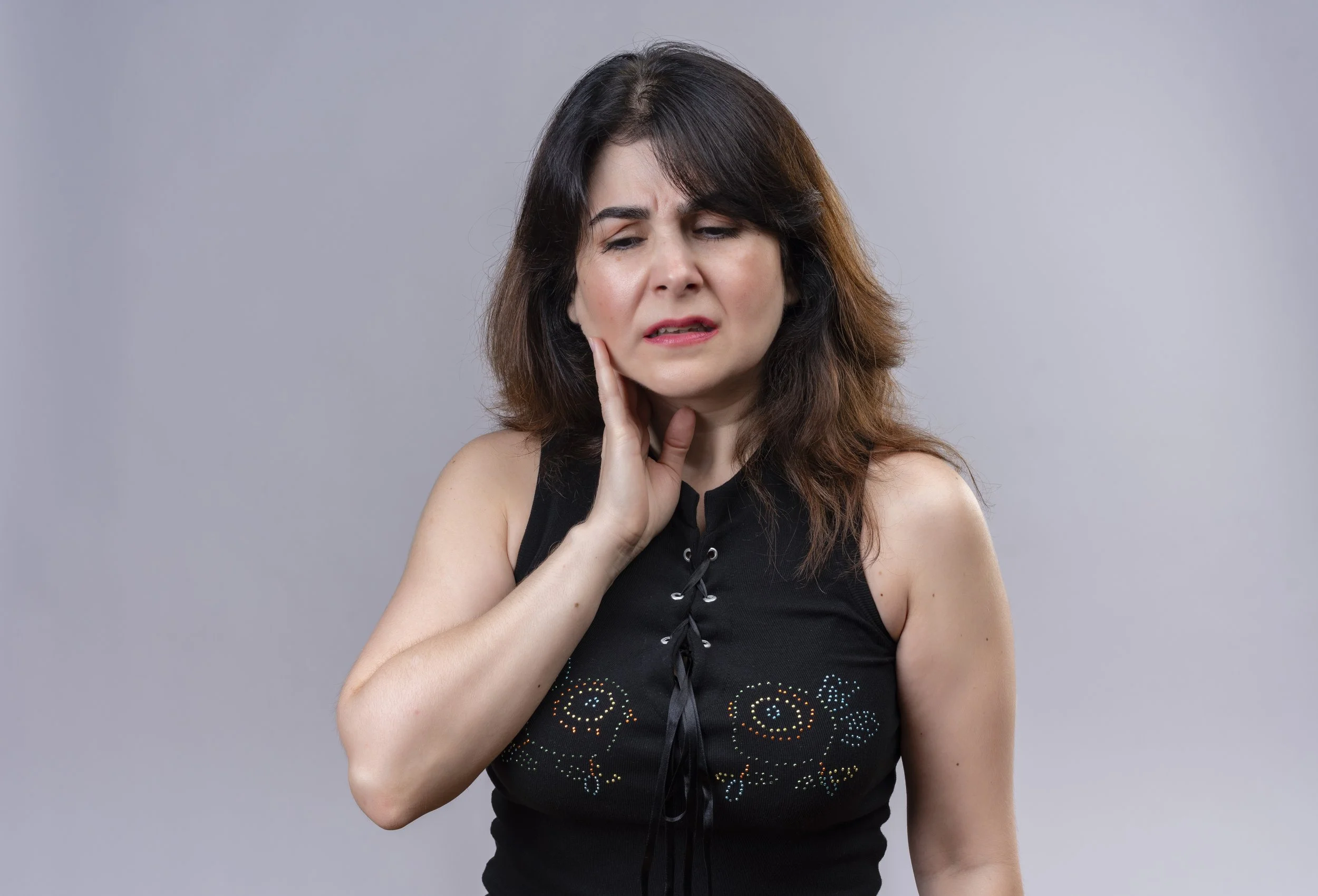 A woman holding her jaw in discomfort, illustrating the facial tension and muscle pain symptoms commonly associated with Temporomandibular Disorder (TMD).