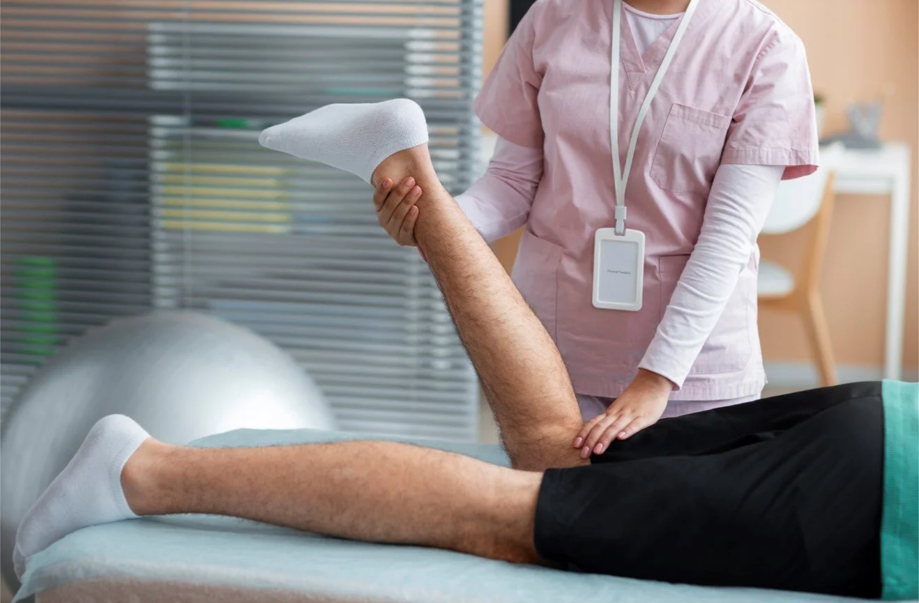 A physical therapist in pink scrubs performing manual knee mobilization and stretching on a patient to restore joint range of motion and reduce pain.