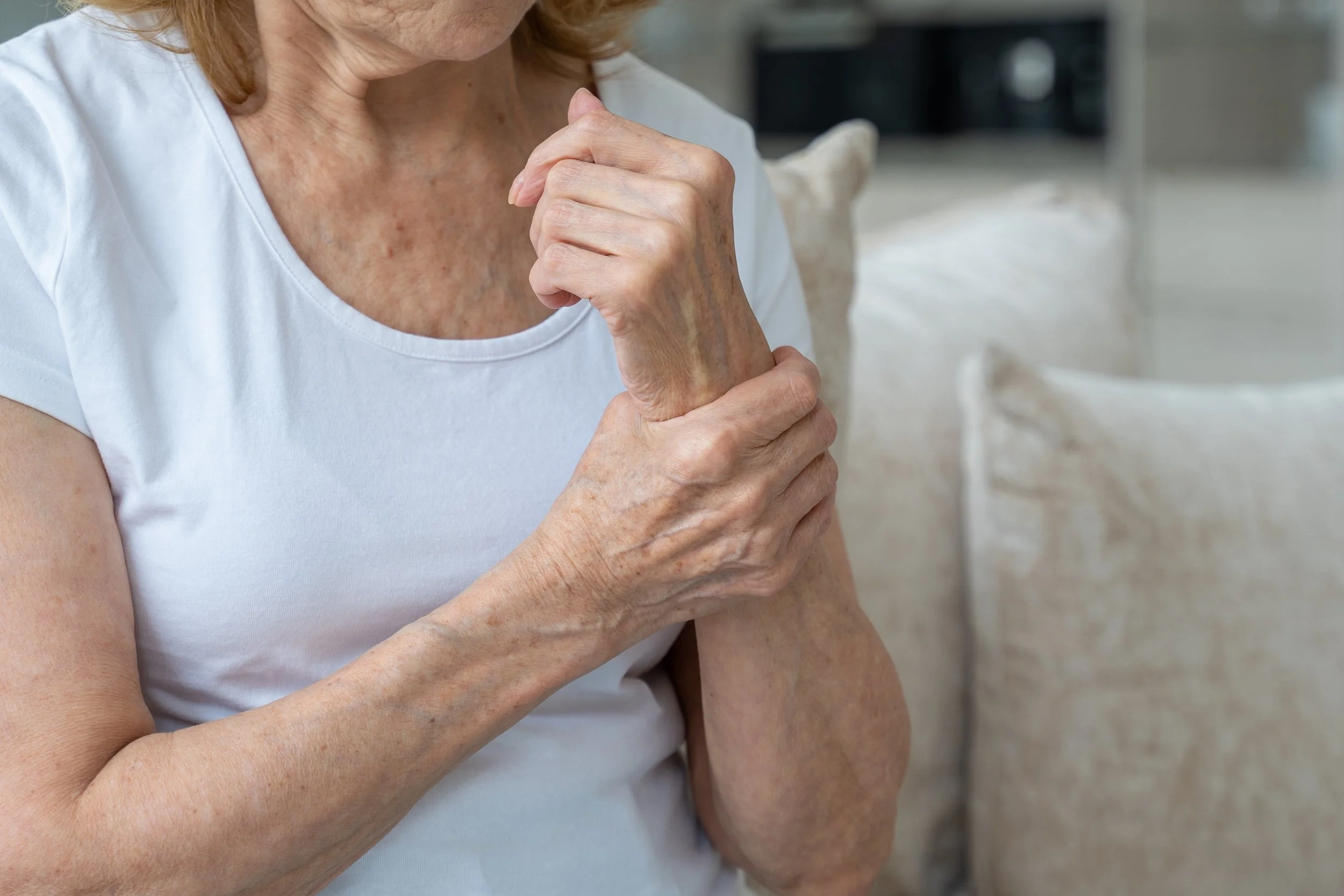 An elderly woman sitting on a sofa clutching her painful wrist and hand, seeking chronic arthritis relief at Signature PT in Manhattan.