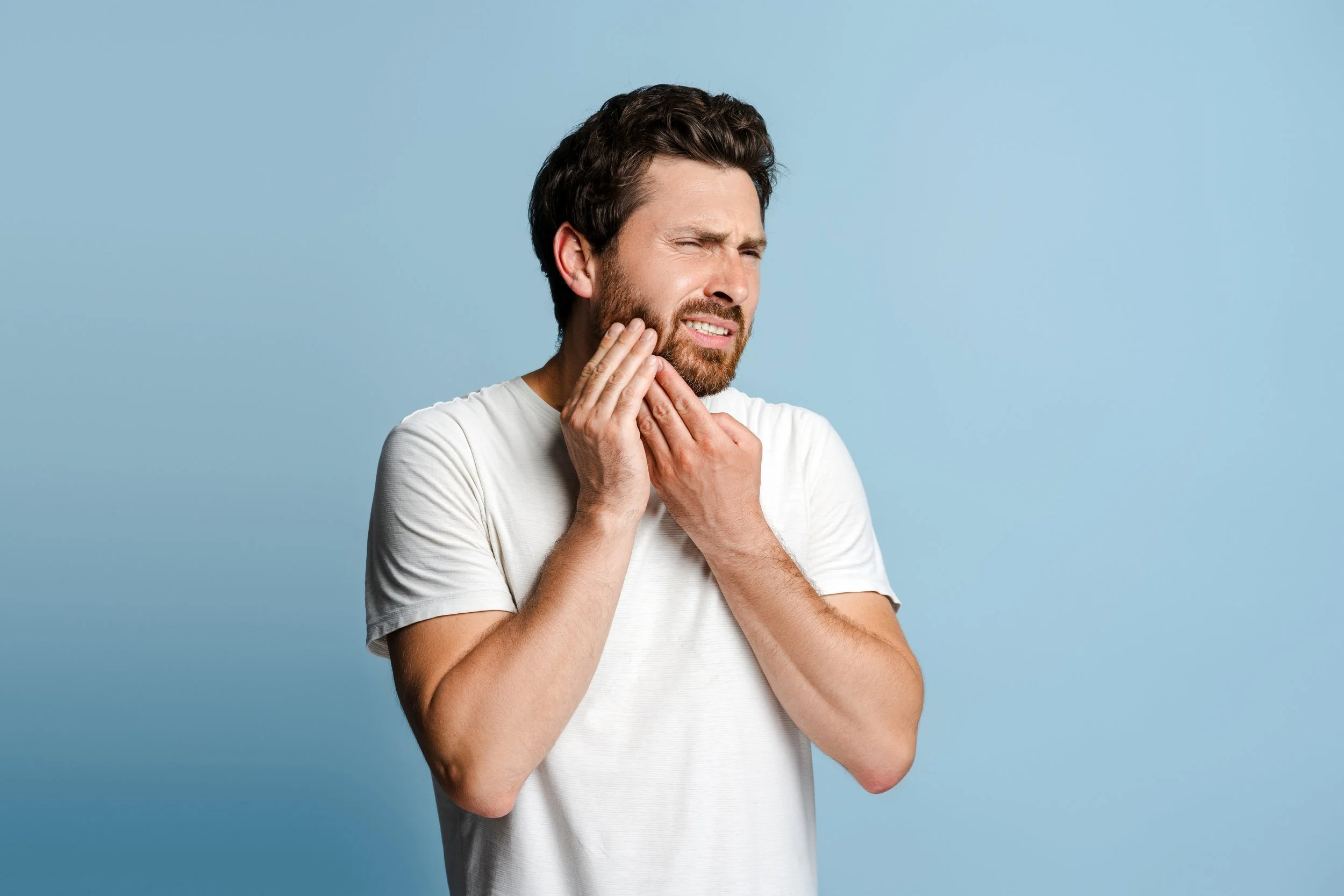 Close-up of a man with short brown hair and a beard suffering from severe jaw pain (TMD), seeking physical therapy in Manhattan at Signature PT.