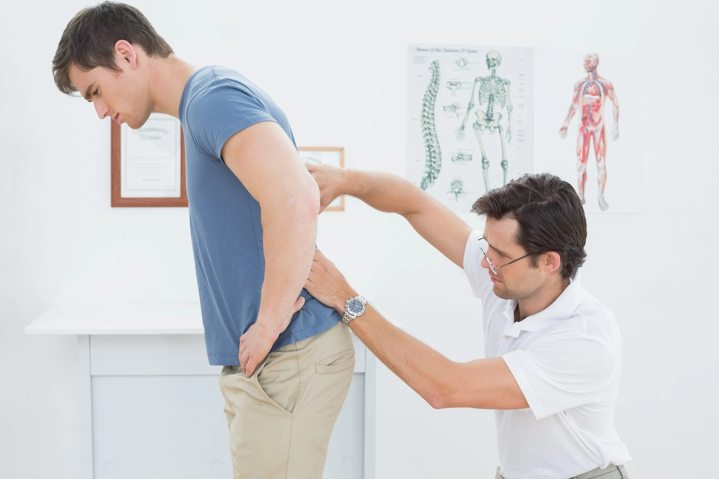 A male physical therapist at Signature PT performing a postural assessment on a patient's spine in a Manhattan clinic to treat slouching and back misalignment.