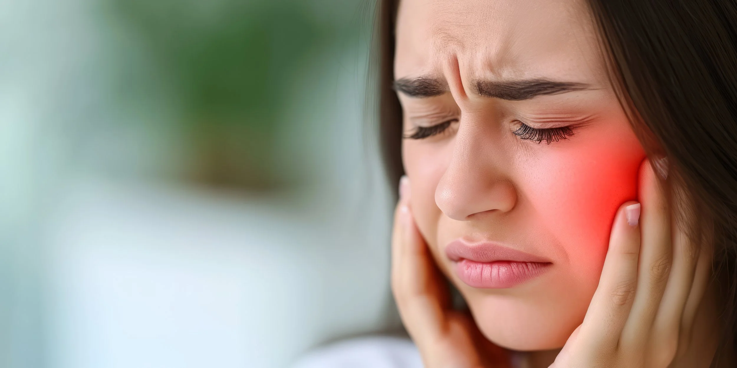 Close-up of a woman clutching her face in pain with a red glow over the temporomandibular joint, seeking TMD and jaw physical therapy in Manhattan.