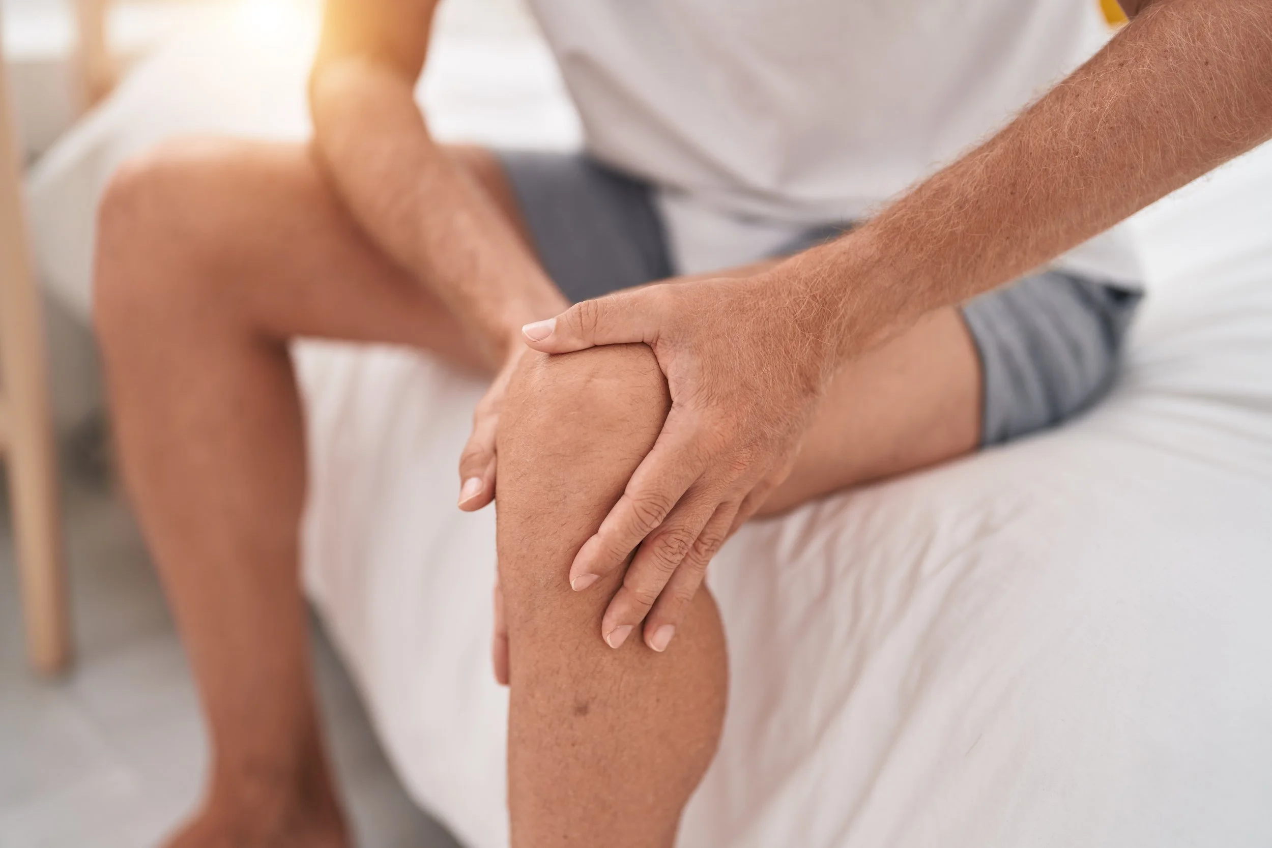 A man suffering from a knee injury clutching his joint, seeking knee pain relief and physical therapy at Signature PT in New York City.