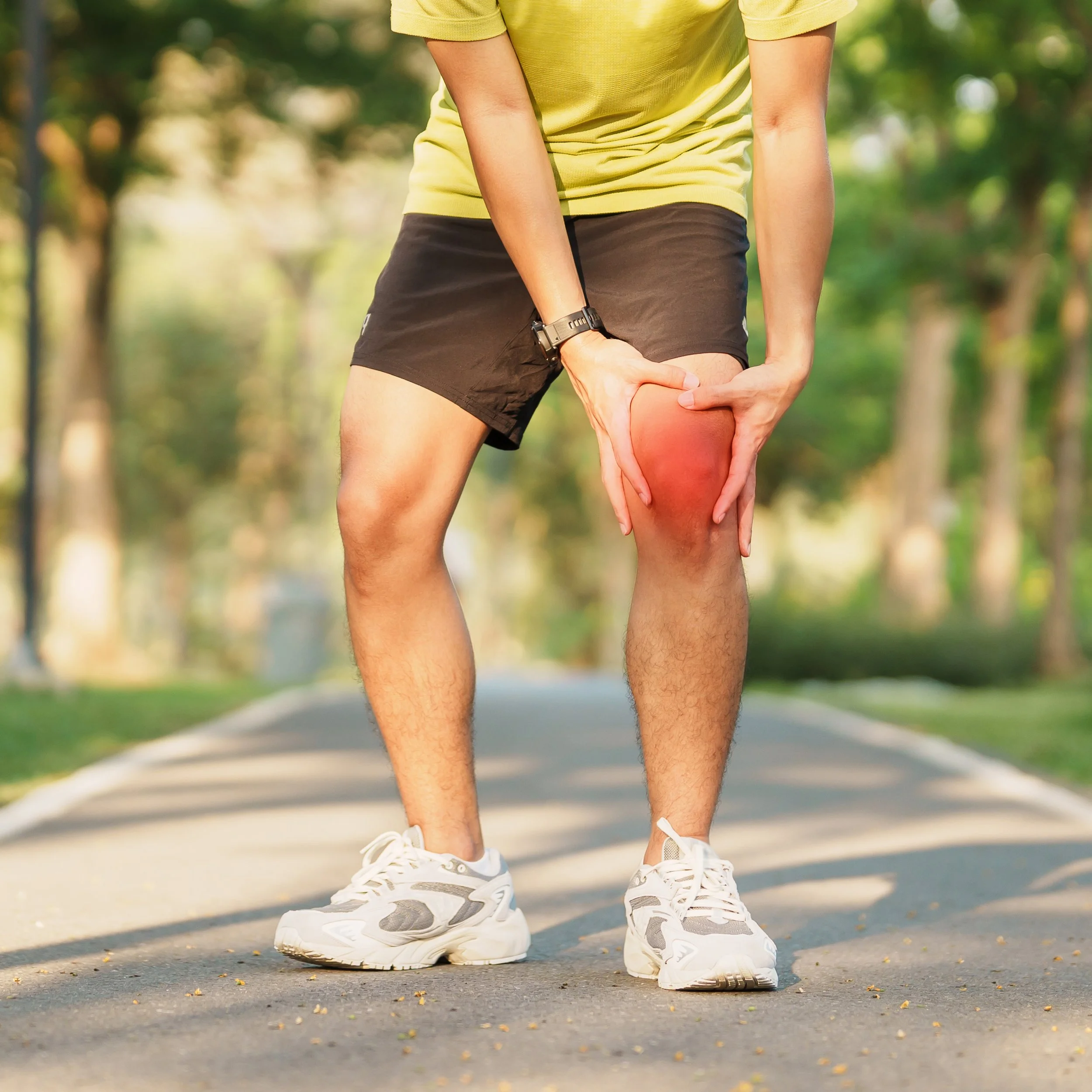 A runner standing on a park path, holding a swollen and painful knee with a red glow overlay, illustrating common causes of athletic injuries.
