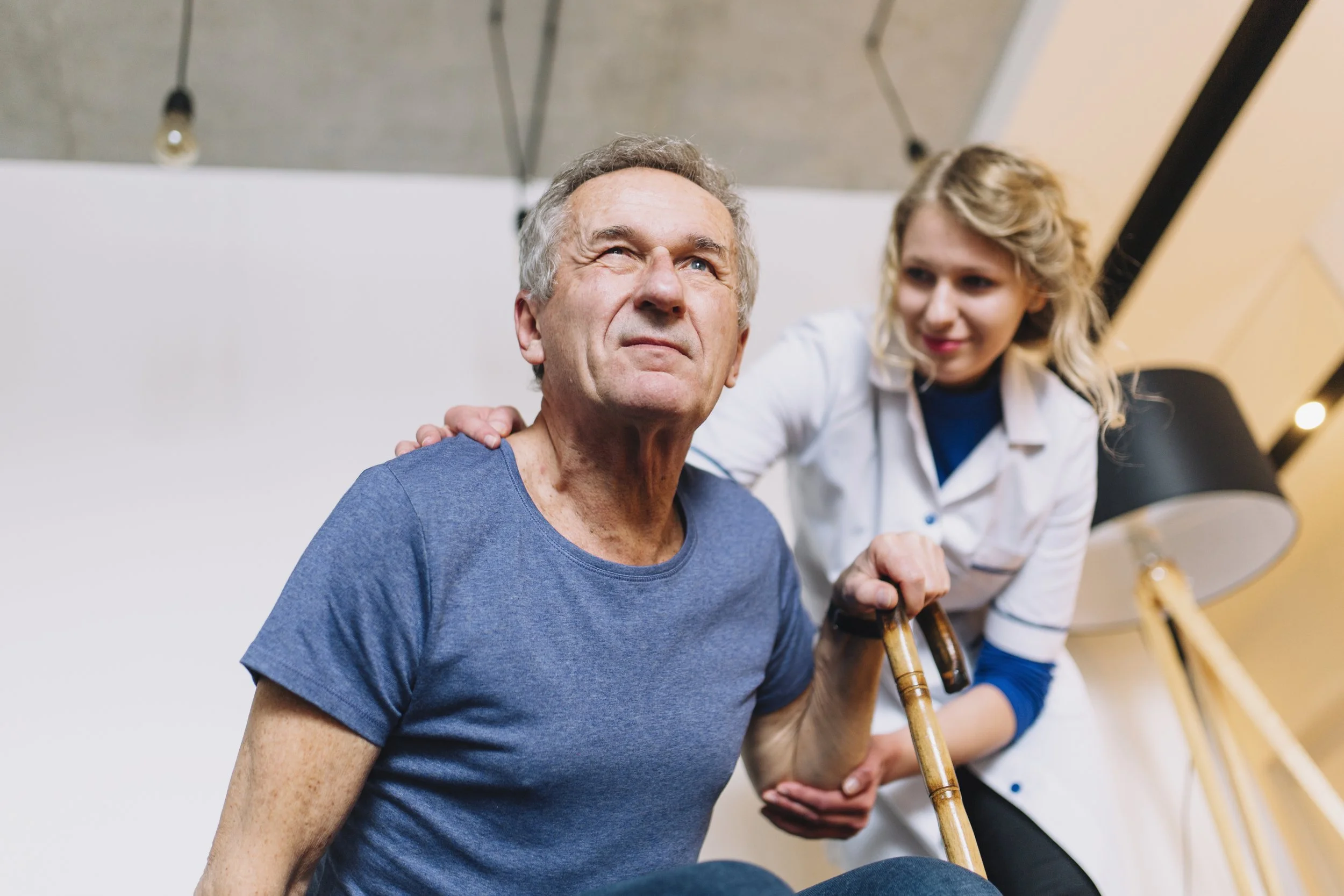 A physical therapist at Signature PT assisting an older man with a cane during stroke rehabilitation in a Manhattan clinic.
