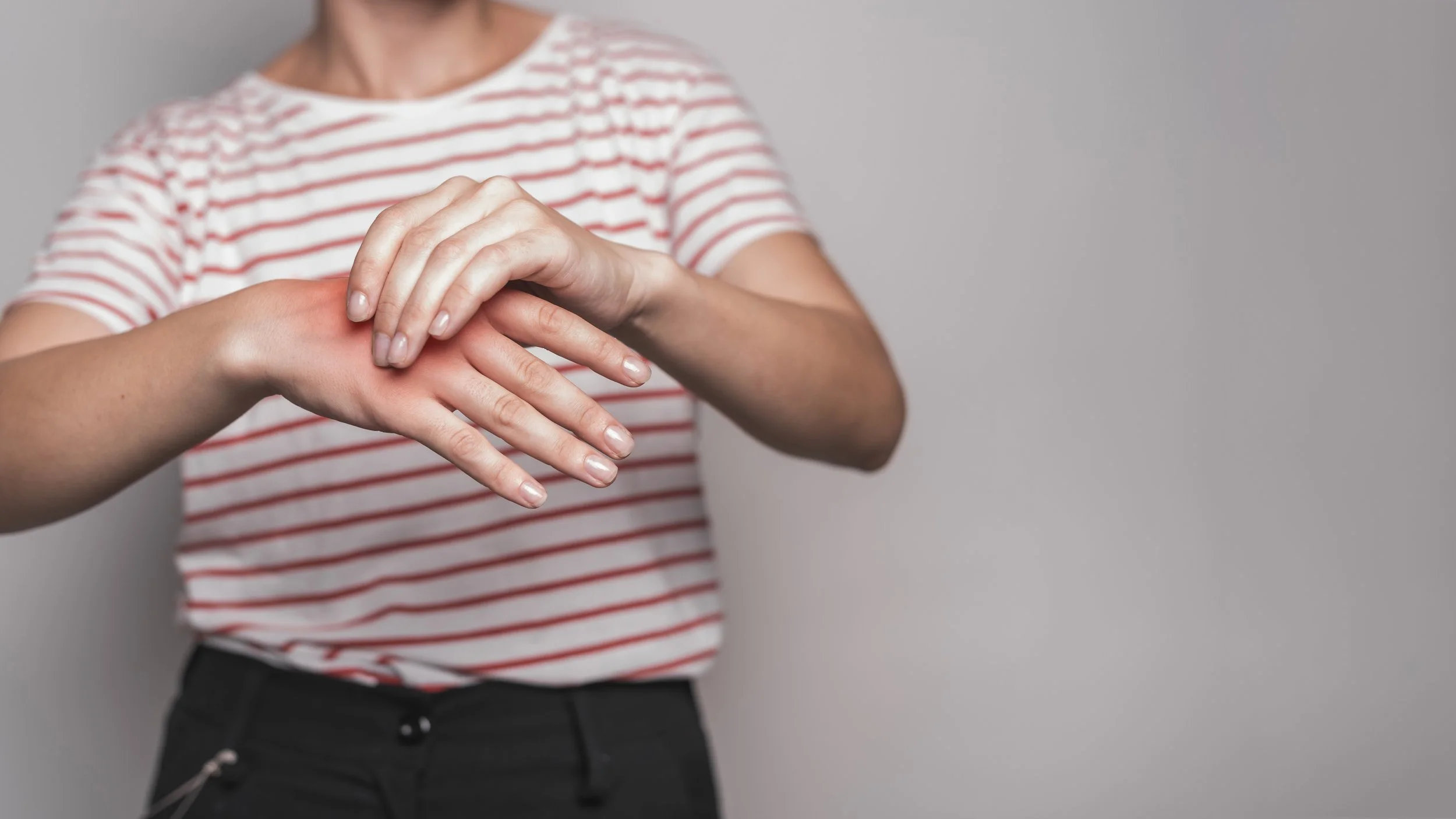 A woman clutching the back of her hand with a red glow overlay, illustrating symptoms of joint inflammation and repetitive strain injuries.