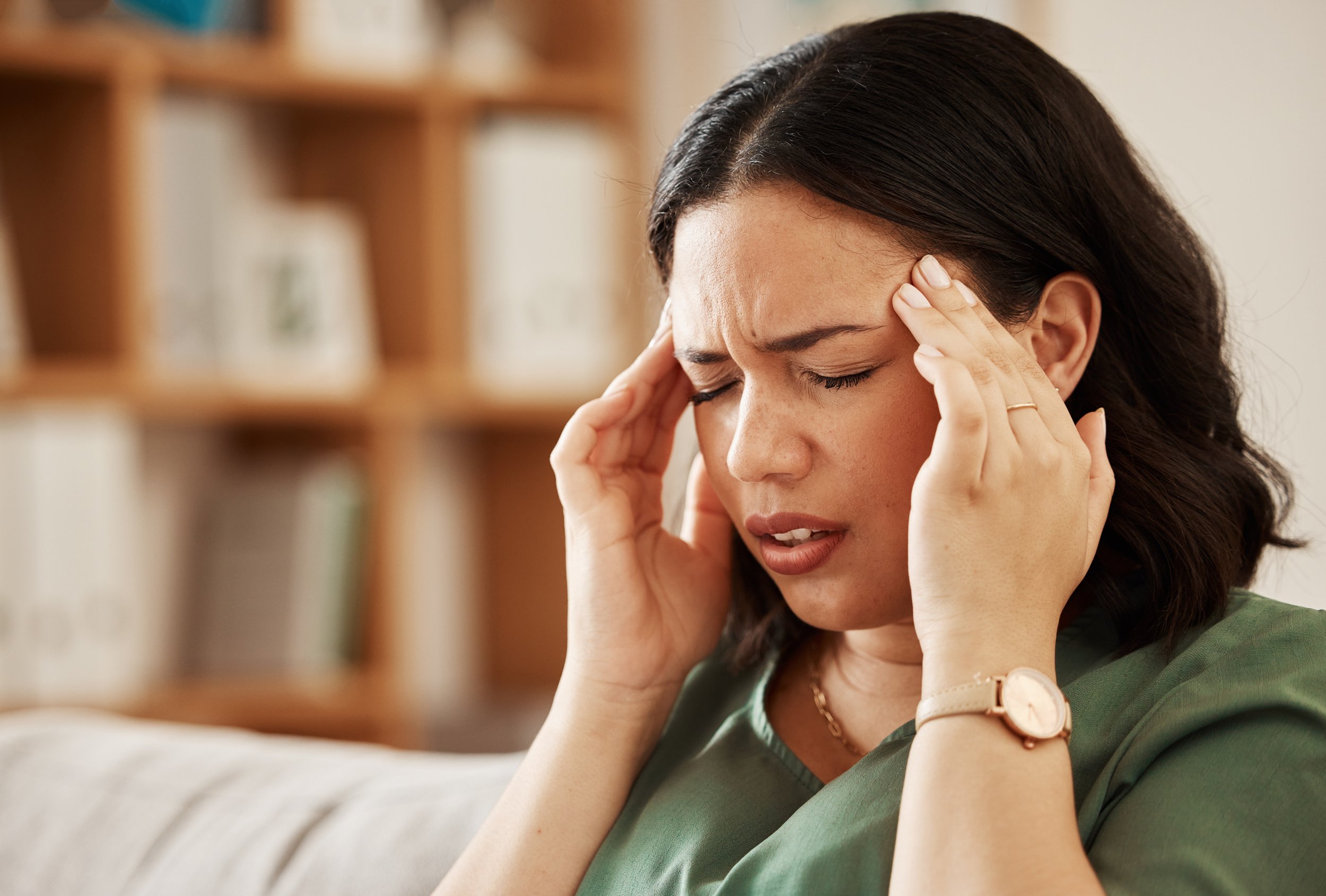 A woman with dark hair holding her temples, illustrating the severe dizziness, spinning sensation, and concentrated strain caused by a vertigo episode.