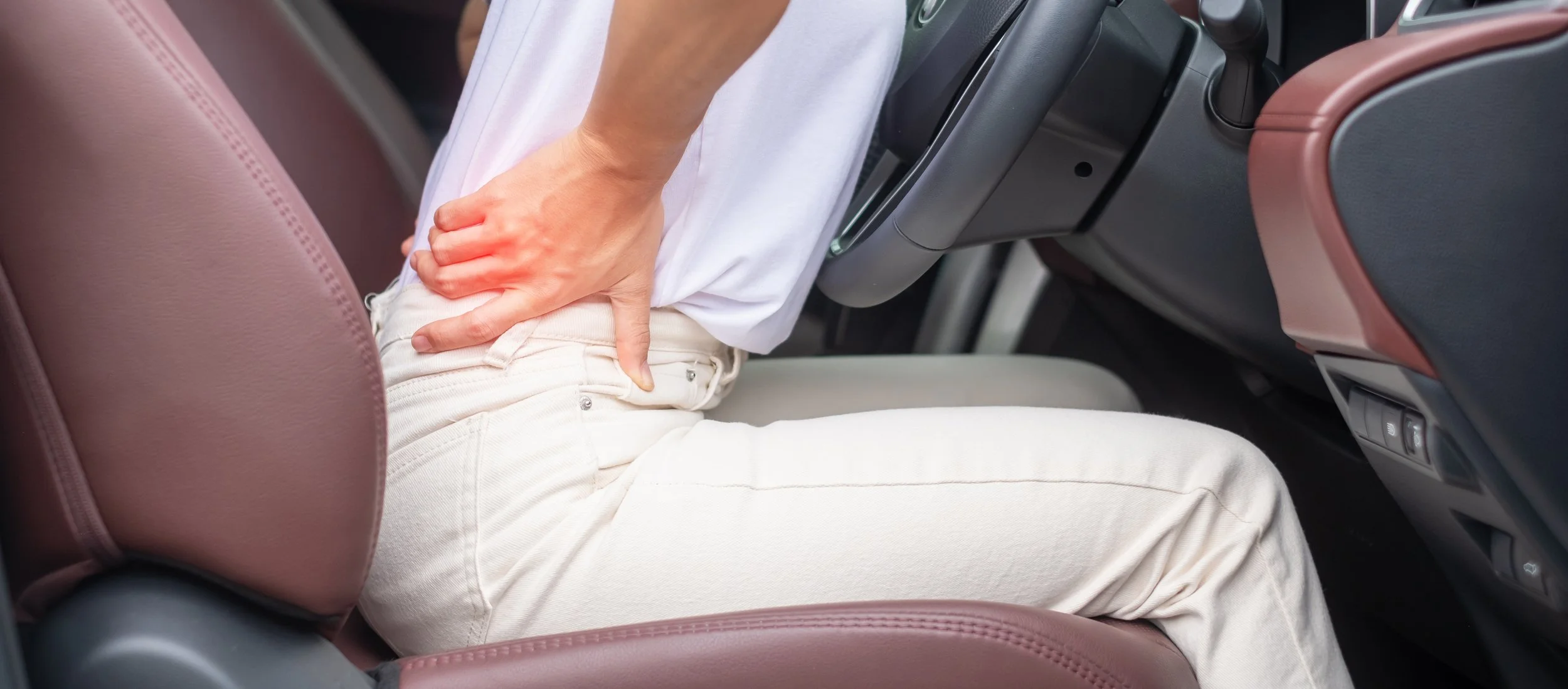A man in a checkered shirt clutching his painful wrist with a red glow indicator while still seated in his car, seeking whiplash and auto injury rehabilitation in Manhattan.