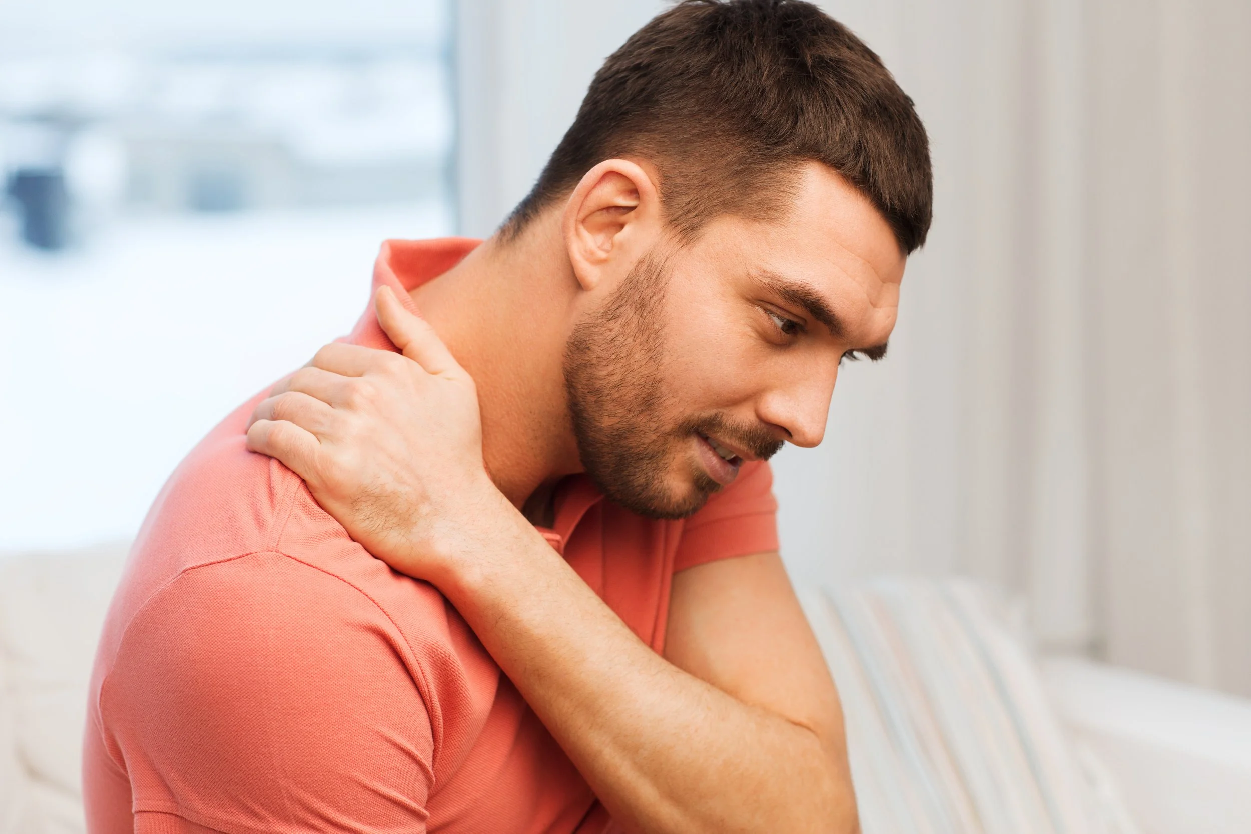 A man in a peach polo shirt clutching his painful shoulder, seeking relief from limited mobility at Signature PT in Manhattan.