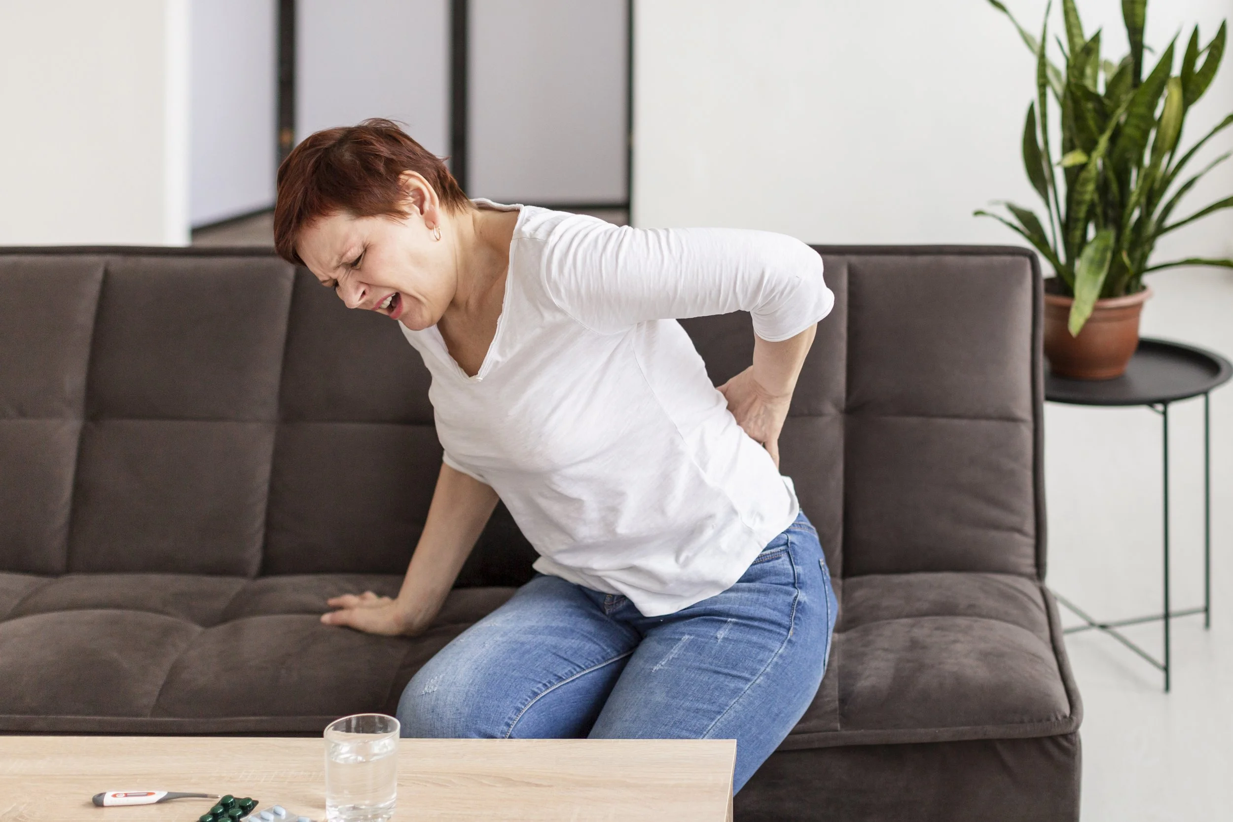 A woman grimacing in pain while holding her lower back, illustrating the severe functional limitations and discomfort caused by spinal curves and deformations.
