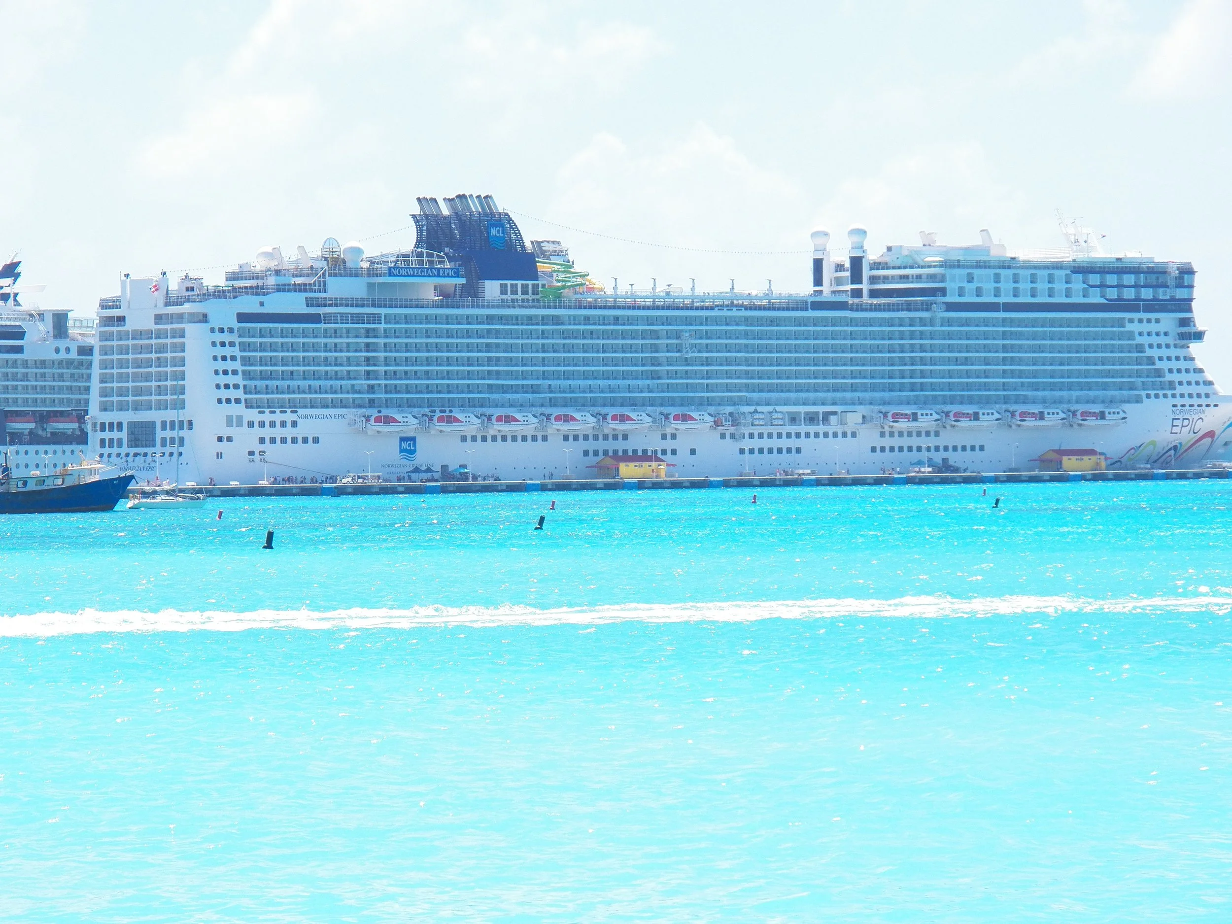 A cruise ship named Norwegian Epic docked in a harbor with bright turquoise water.