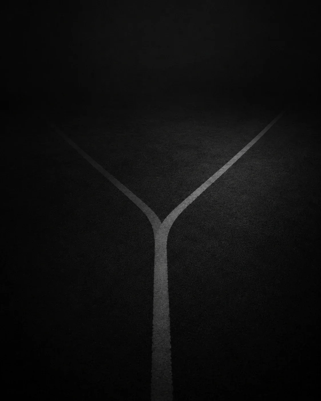 Marquage routier clair se séparant en Y sur une chaussée sombre, symbolisant les choix stratégiques d'un dirigeant d'entreprise
