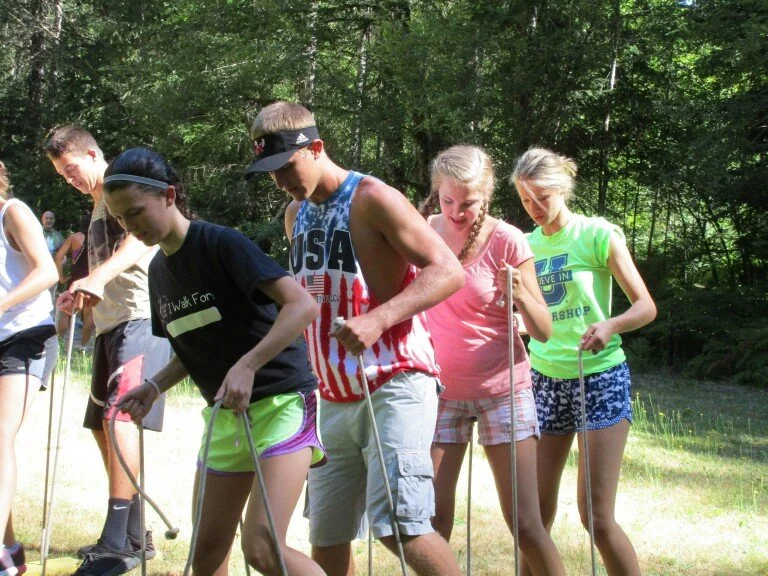 Group of teenagers outdoors in a wooded area participating in a team-building activity with ropes.
