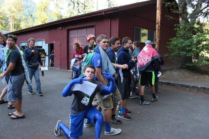 Group of teenagers waiting in line outside a red building surrounded by trees.
