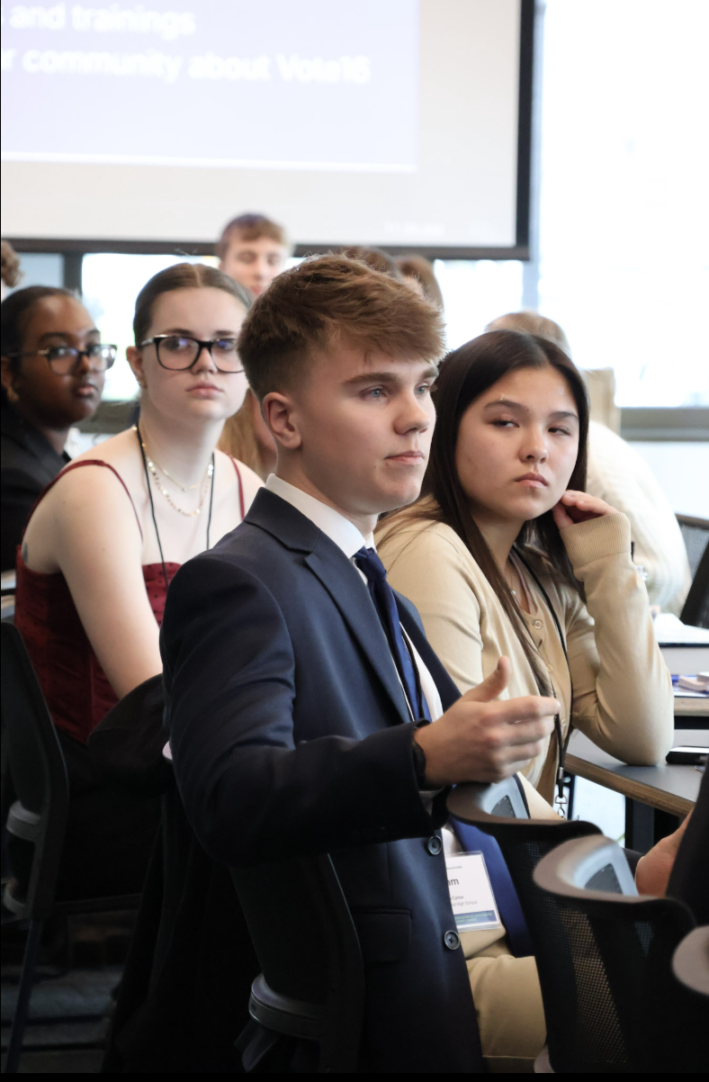 A group of young adults attending a conference or presentation in a classroom or conference room.
