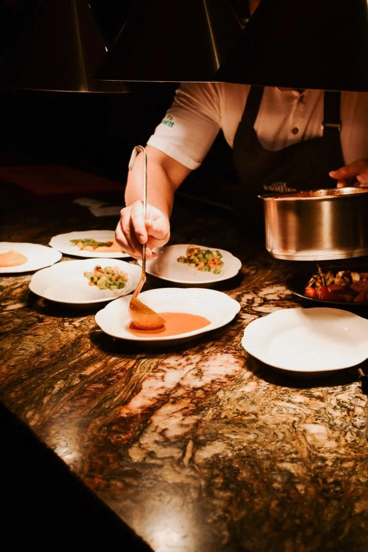 Chef sirviendo salsa en platos con comida en una cocina profesional.