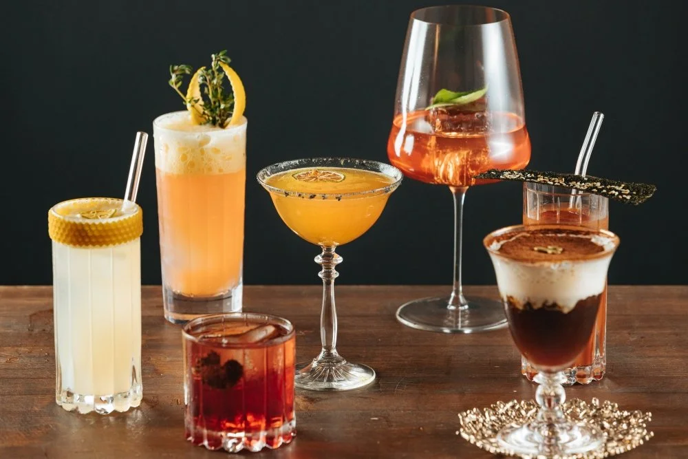 Variedad de cócteles coloridos en copas y vasos sobre una mesa de madera 