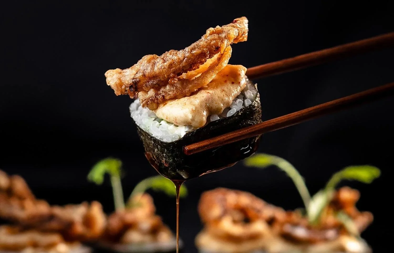 Un trozo de sushi con arroz, alga nori, y mariscos, con salsa oscura y palillos