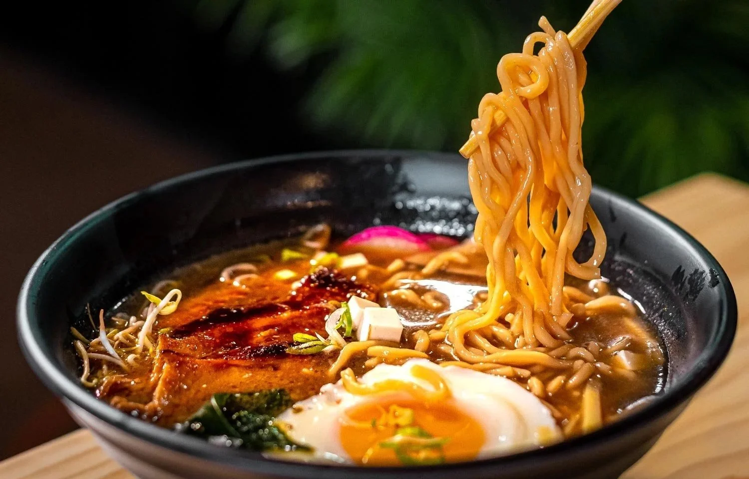 Un tazón con ramen, fideos amarillos, un huevo poche, vegetales, salsa y otros ingredientes en un caldo oscuro