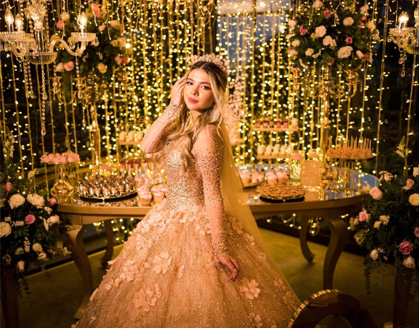 Juvenil mujer con vestido de gala en tonos dorados con detalles de flores y brillo, en fiesta decorada con luces, flores y candelabros dorados.