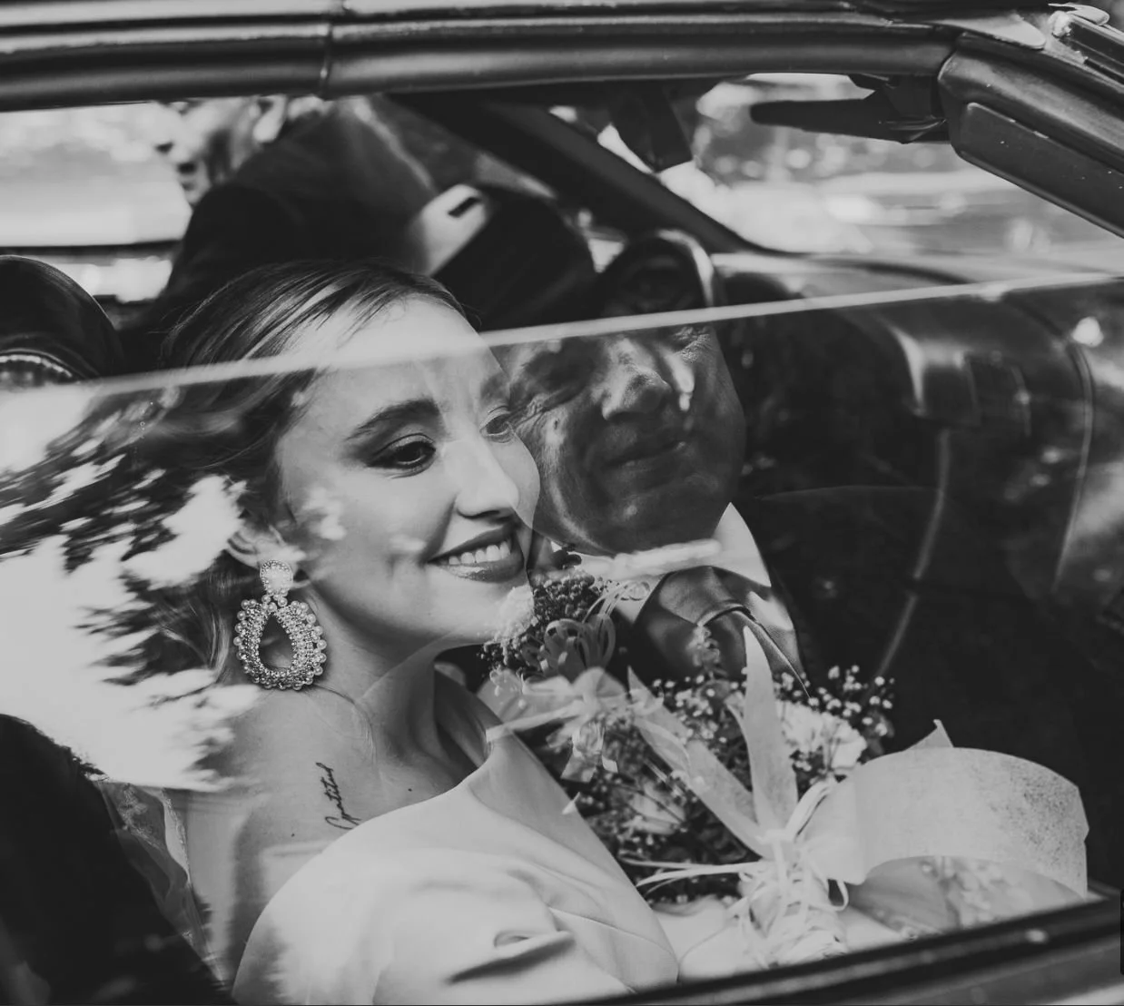 Pareja de novios en un coche clásico en su boda, sonríen y están vestidos con ropa formal.