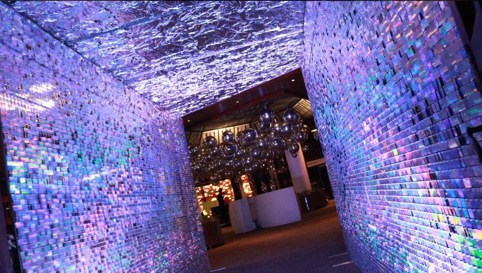 Puertas decorativas con mosaicos de cristales que reflejan luces violetas y azules, en un espacio con iluminación ambiental y decoraciones modernas.