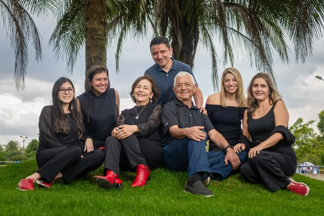 Un grupo de ocho personas, mayores, jóvenes y niños, posan juntas en un parque con palmeras y cielo nublado, en una foto familiar.