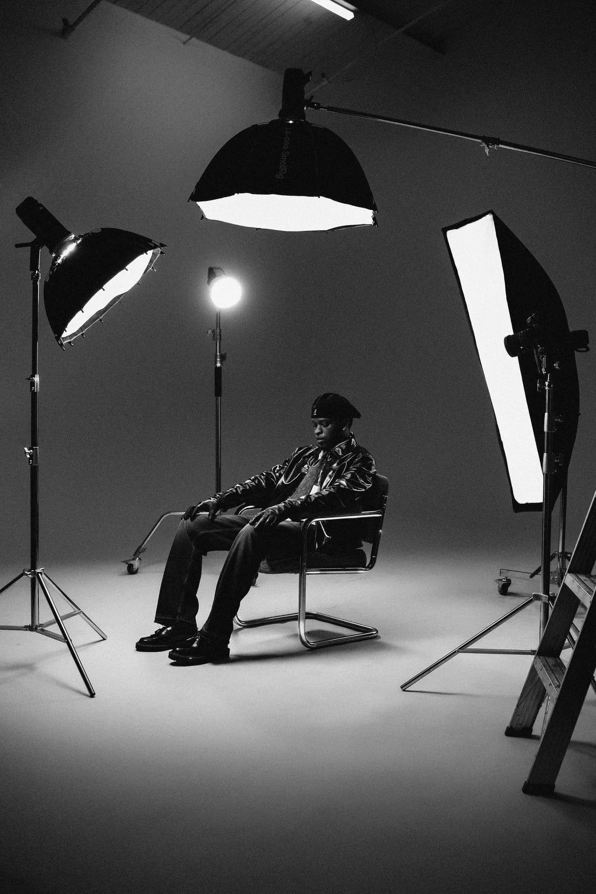 Persona sentada en una silla en un estudio fotográfico con equipo de iluminación y reflectores negros y blancos.