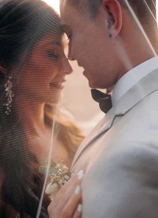 Pareja de recién casados tocándose en una ceremonia de boda, con un fondo natural y cálido.