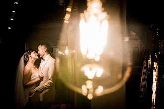 Una pareja de novios mirándose íntimamente en un entorno oscuro, con una lámpara de luz cálida en primer plano.