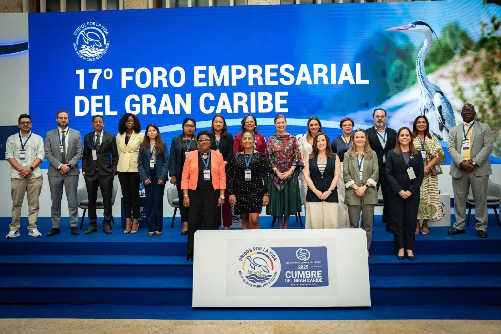 Grupo de personas posando en un escenario frente a un cartel azul que dice '17° Foro Empresarial del Gran Caribe' con un logotipo de un ave y la frase 'Unidos por la Vida'.