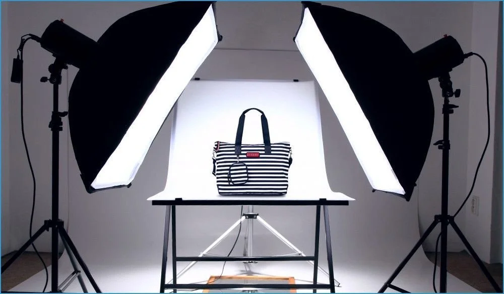 Configuración de fotografía de productos con varias luces y fondo blanco, mostrando una bolsa de rayas negras y blancas en un escritorio.