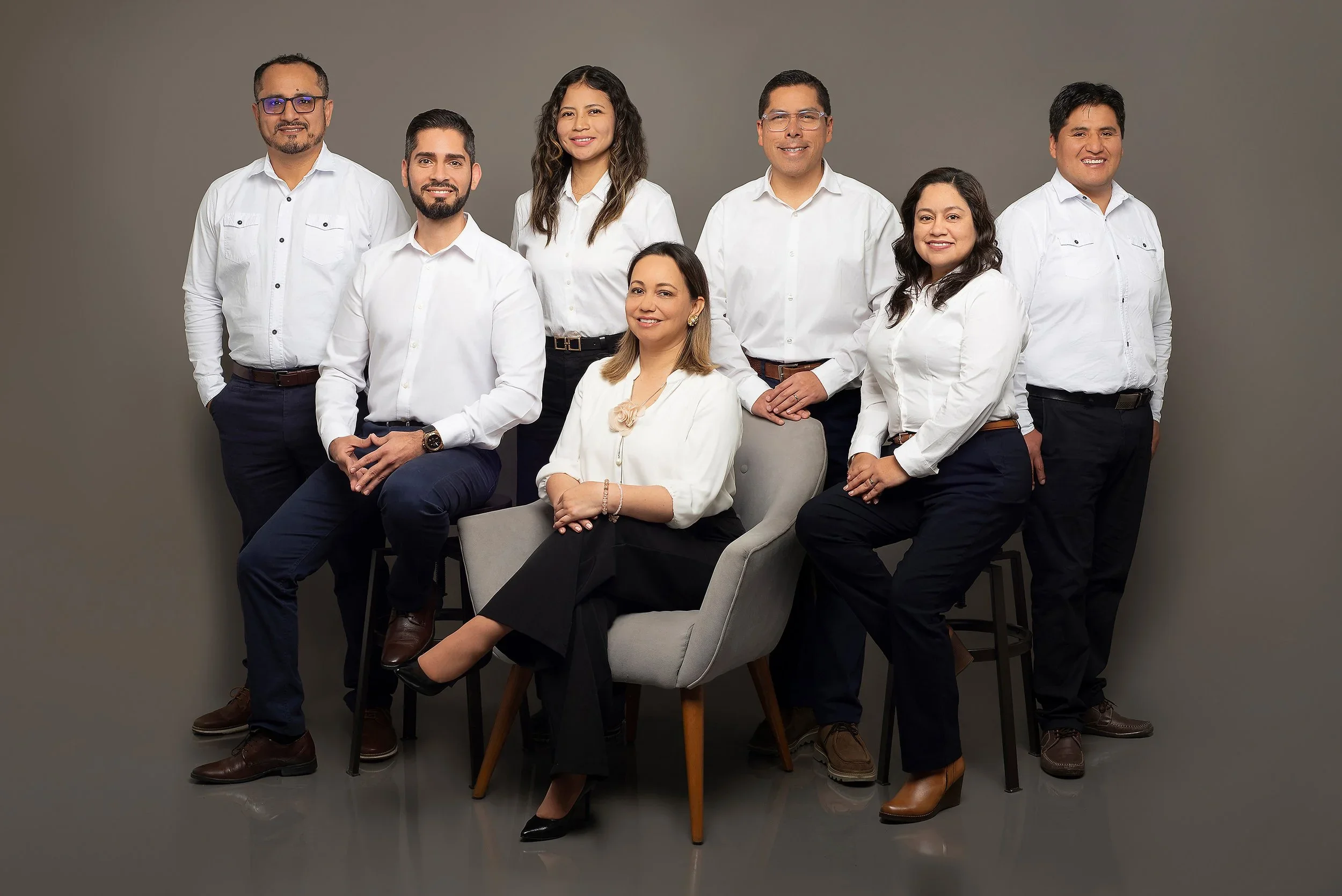 Grupo de ocho personas en ropa formal posando contra fondo gris.