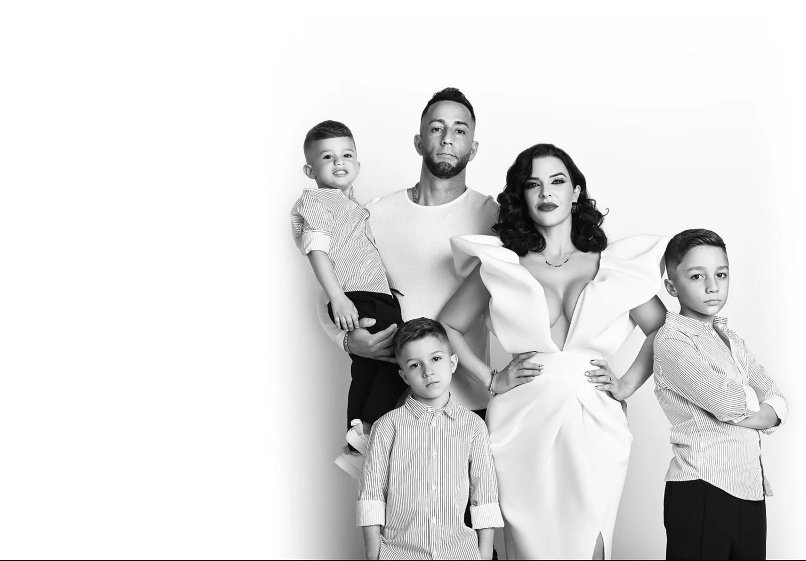 Una familia de cinco personas en blanco y negro, con dos niños pequeños, un hombre y una mujer, todos con expresiones serias o neutrales, de pie contra un fondo blanco.