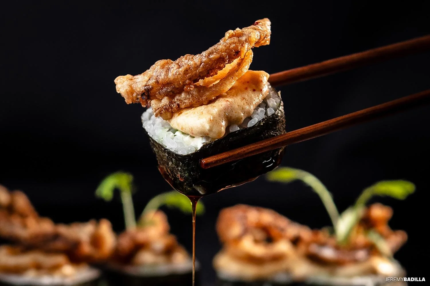 Un trozo de sushi con arroz, alga nori, y mariscos, con salsa oscura y palillos